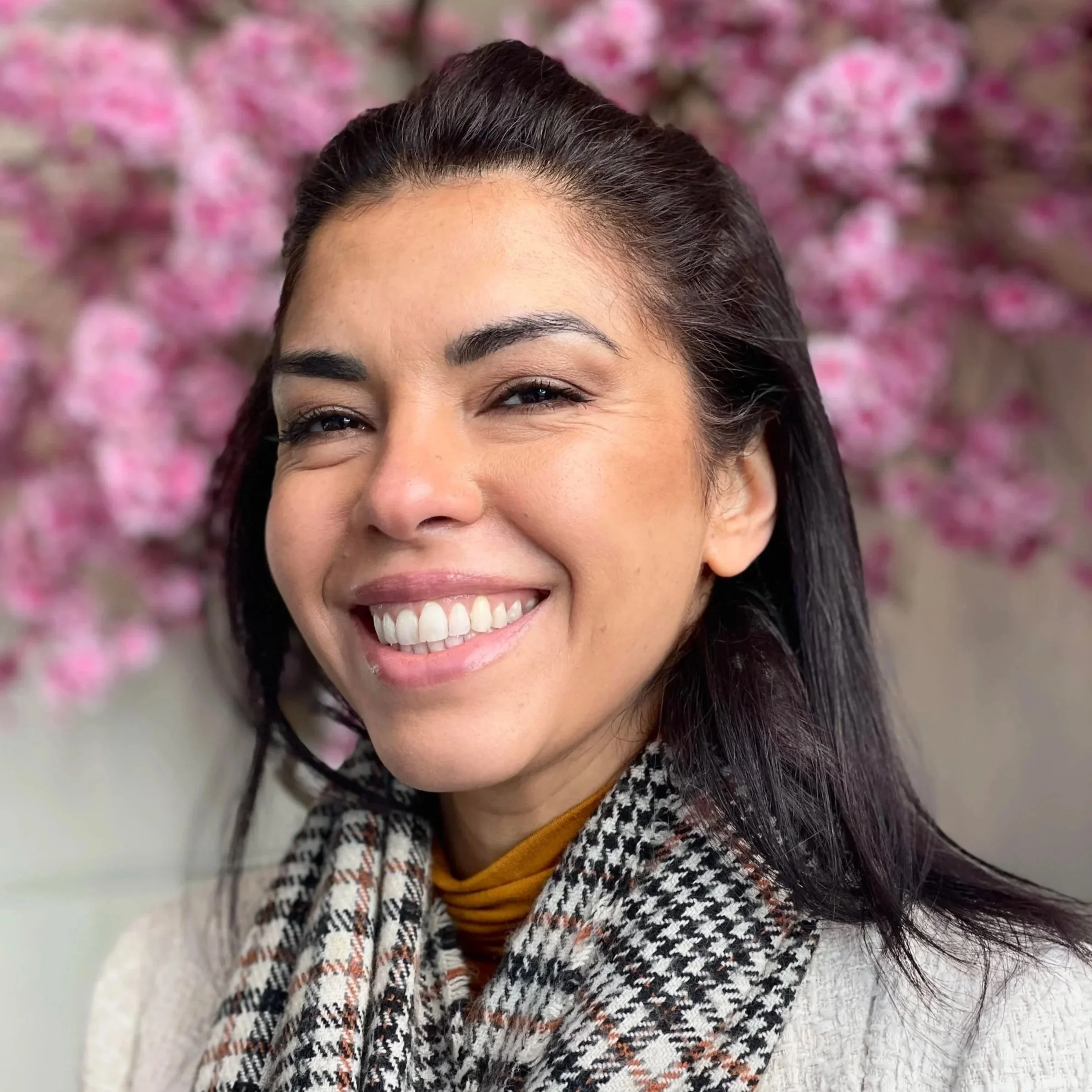 A woman smiling with pink blossoms in the background.