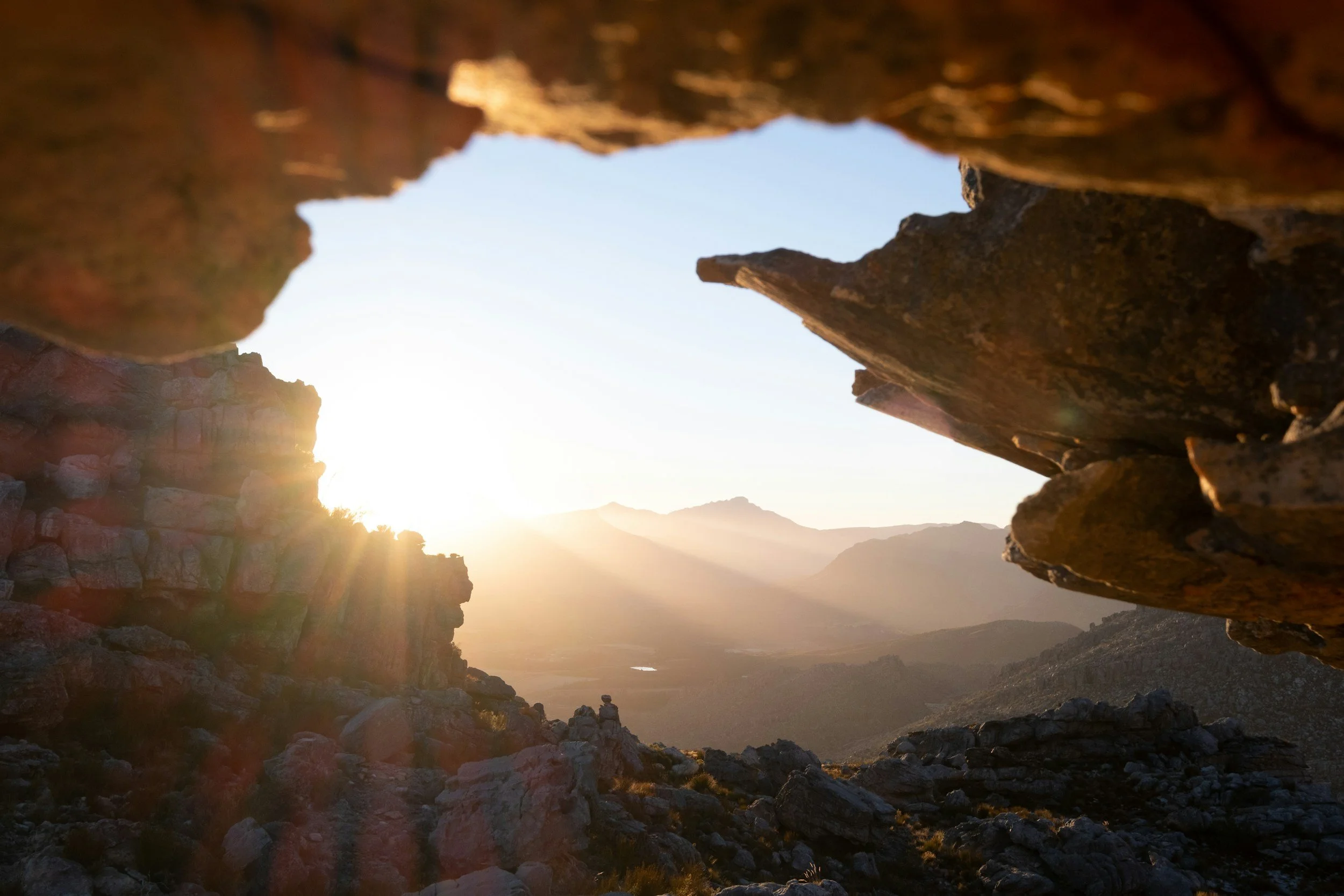 Sunset shining over a mountainous landscape viewed through a rocky crevice.