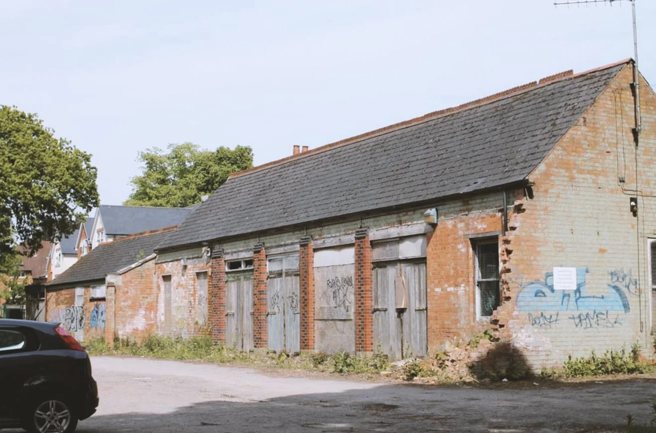 An old, abandoned brick building with boarded windows and graffiti on the walls.