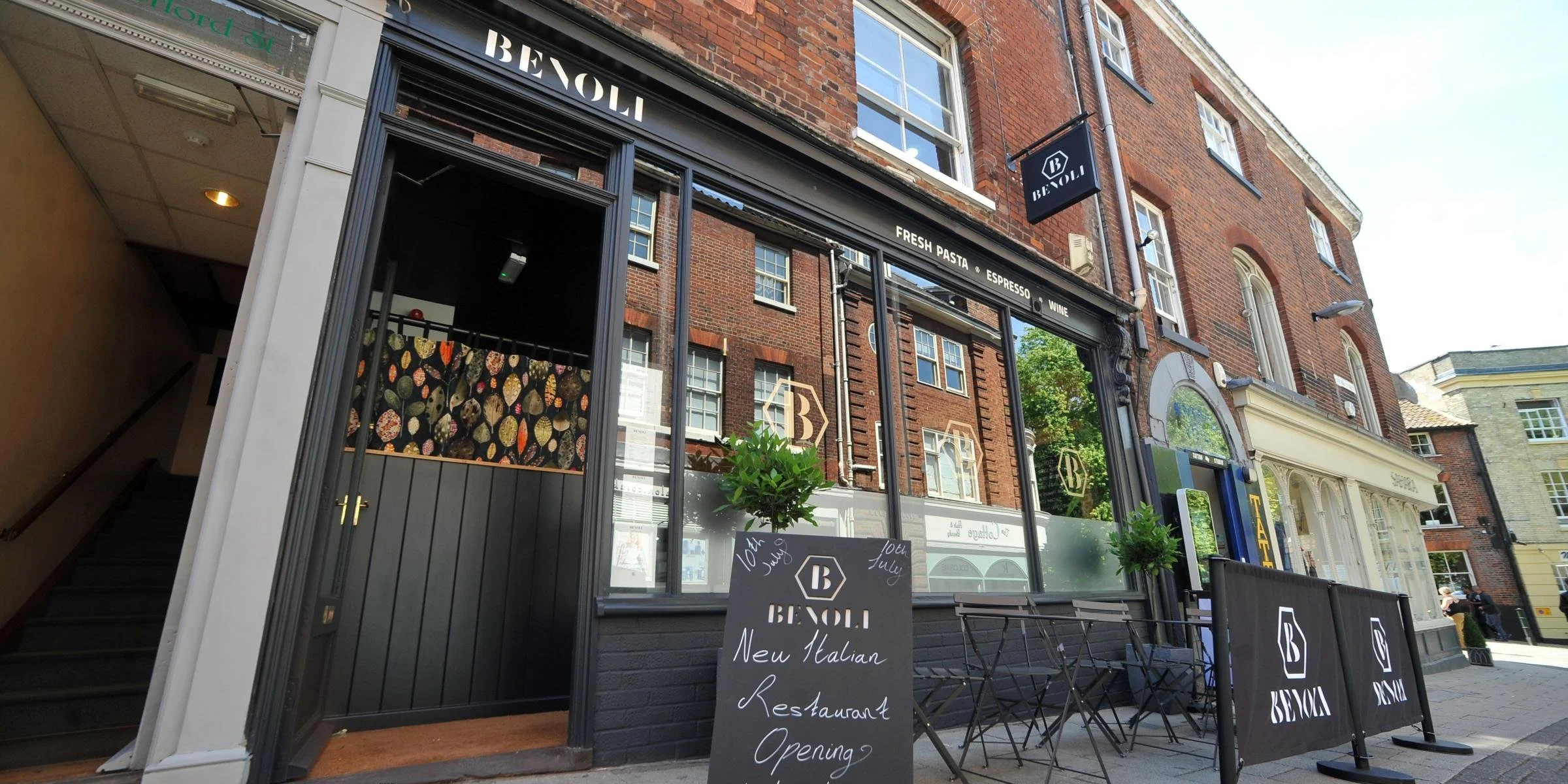 Facade of St. Giles Pantry in Norwich, a general store with floral decorations, a bicycle parked outside, and wooden outdoor seating.