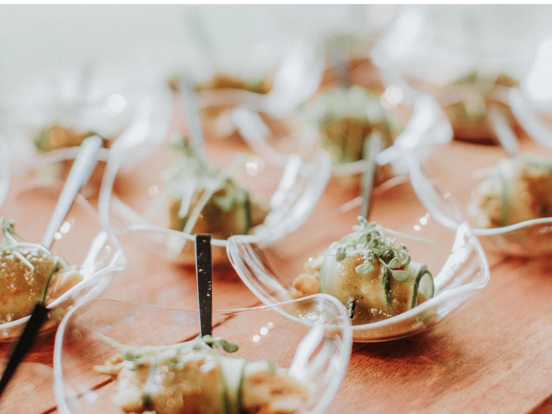 Appetizer of small savory bites with microgreens in clear glass spoons on a wooden surface.