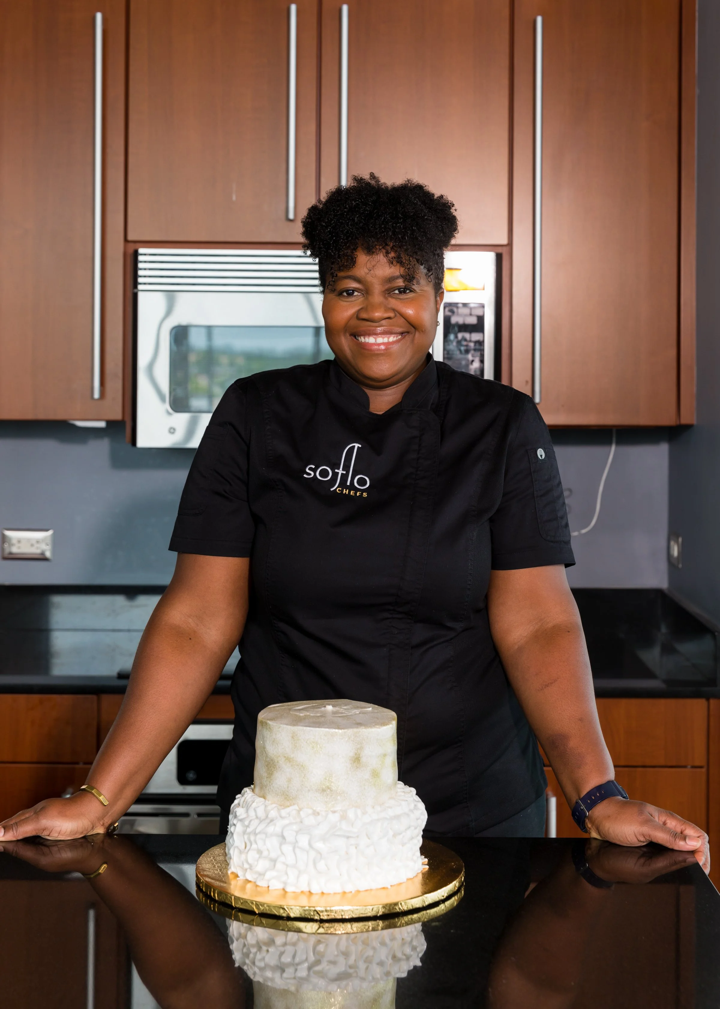 Chef Norma of Soflo Chefs standing in kitchen with decorated cake, showcasing personalized cuisine.