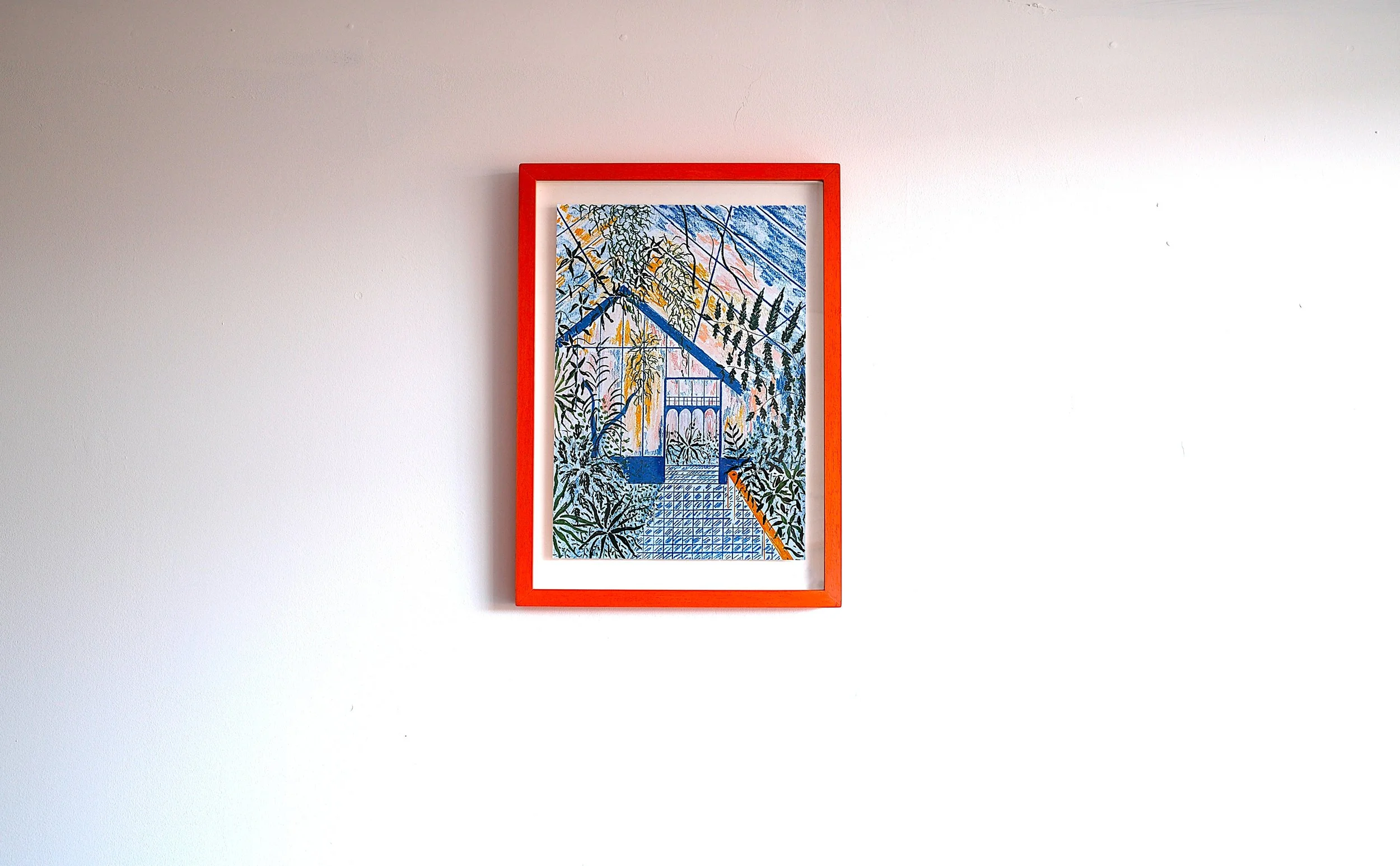 Framed colorful artwork hanging on a plain white wall, depicting a detailed scene with plants and architectural elements.