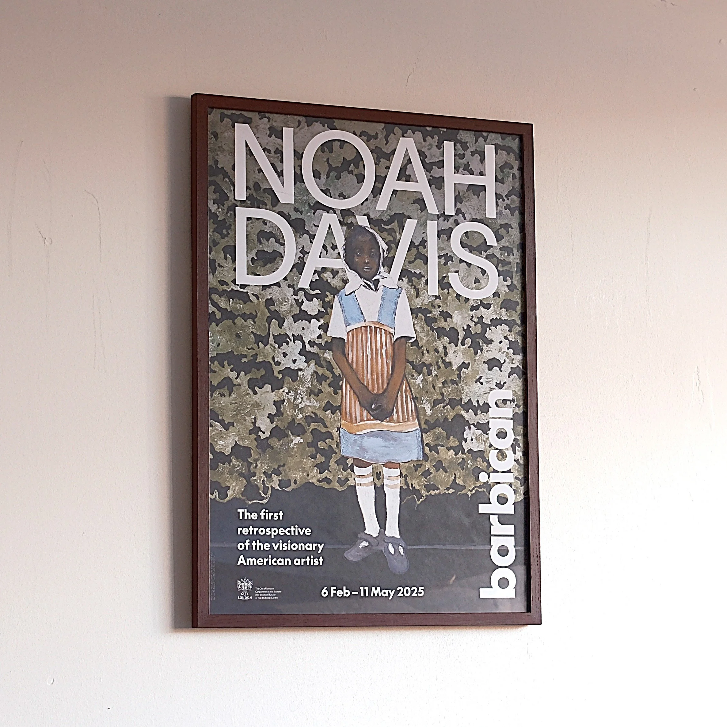 Poster featuring a young girl in a dress with striped sleeves and apron, standing in front of a camouflage background, promoting an exhibition about Noah Davis, artbayinci.com, taking place from February 6 to May 11, 2025.