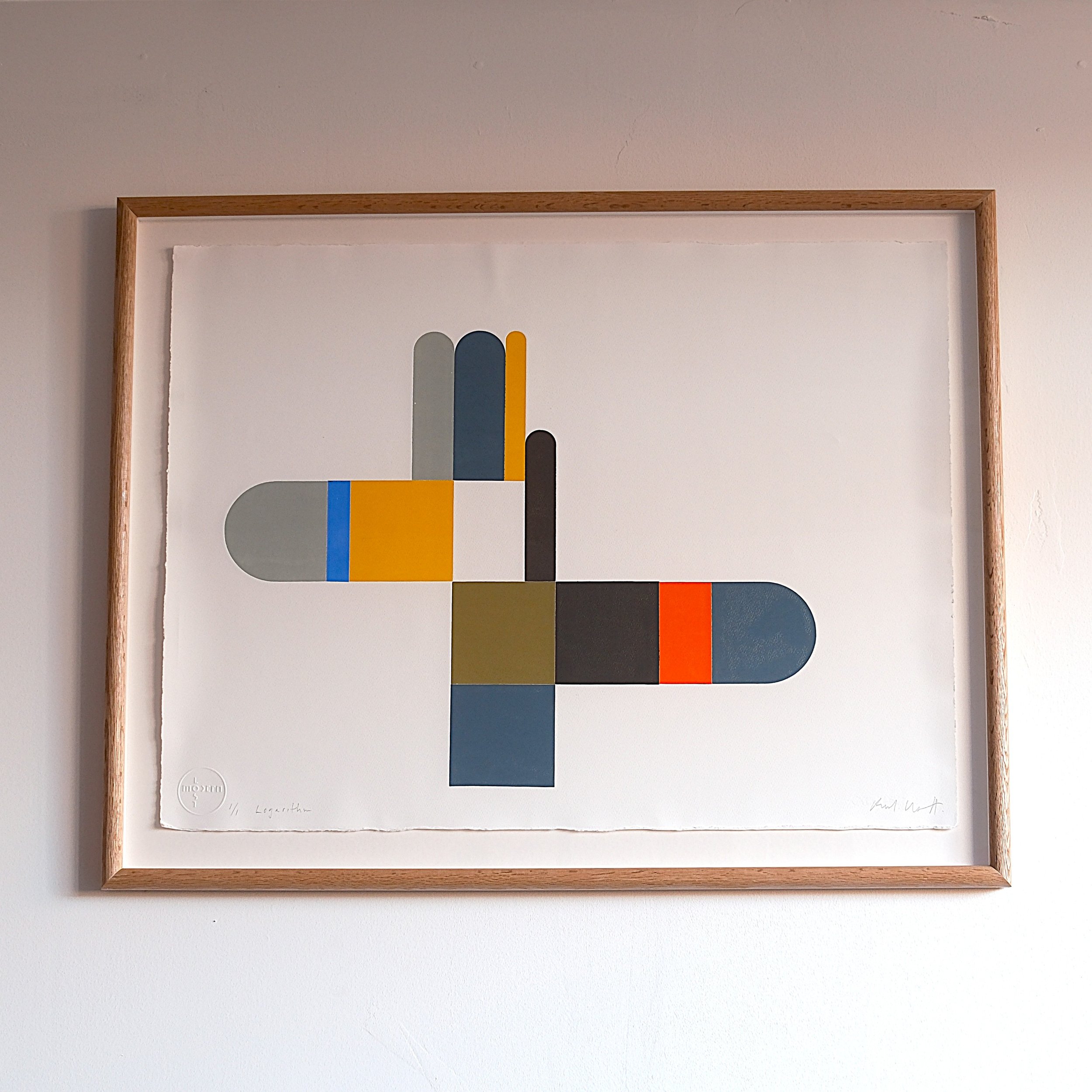 Abstract geometric artwork featuring colorful rectangular and oval shapes on a white background, framed in wood.