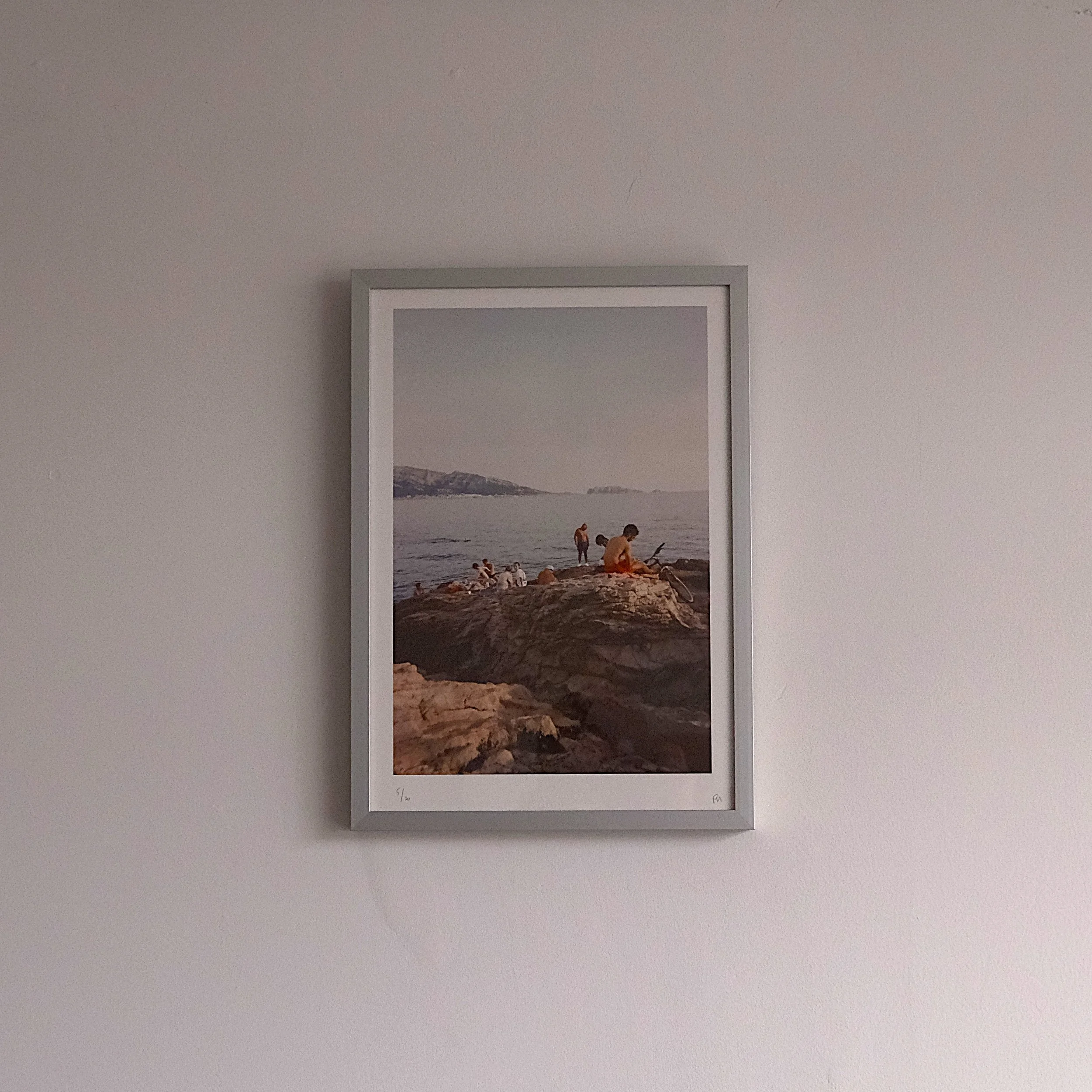 Photograph of people sitting and relaxing on rocky shore by the sea at sunset.