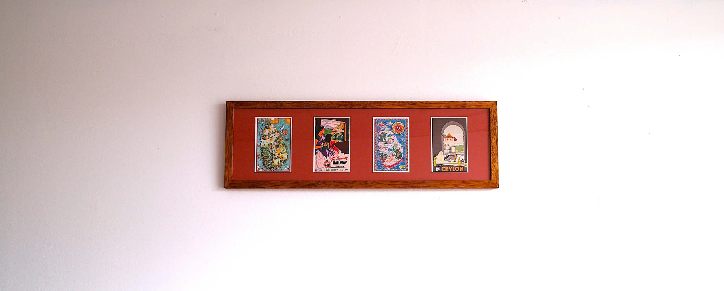 A framed display with four vintage travel posters on a red background hung on a white wall.
