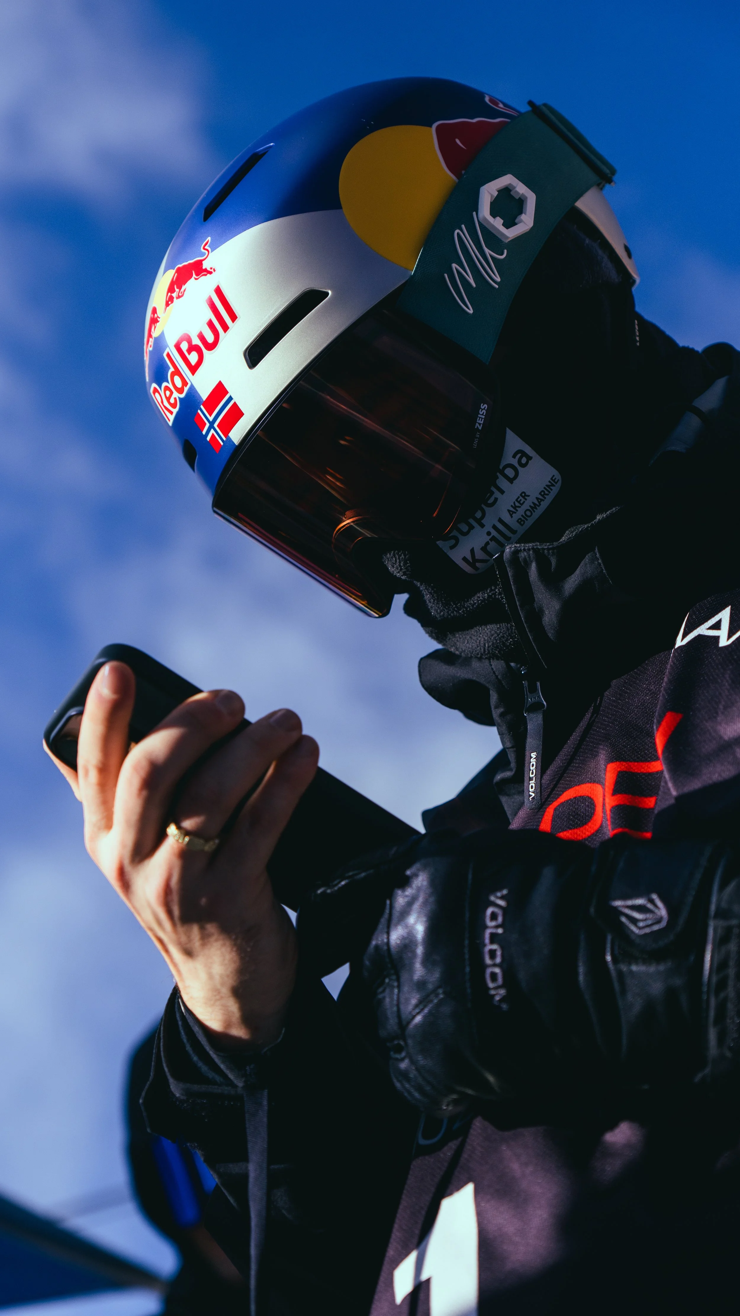 Close-up of a person wearing a helmet with Red Bull and Alpine logos, looking at a smartphone.