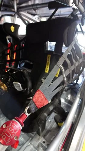 A fire extinguisher attached to a racing vehicle's roll cage with a gray safety strap.
