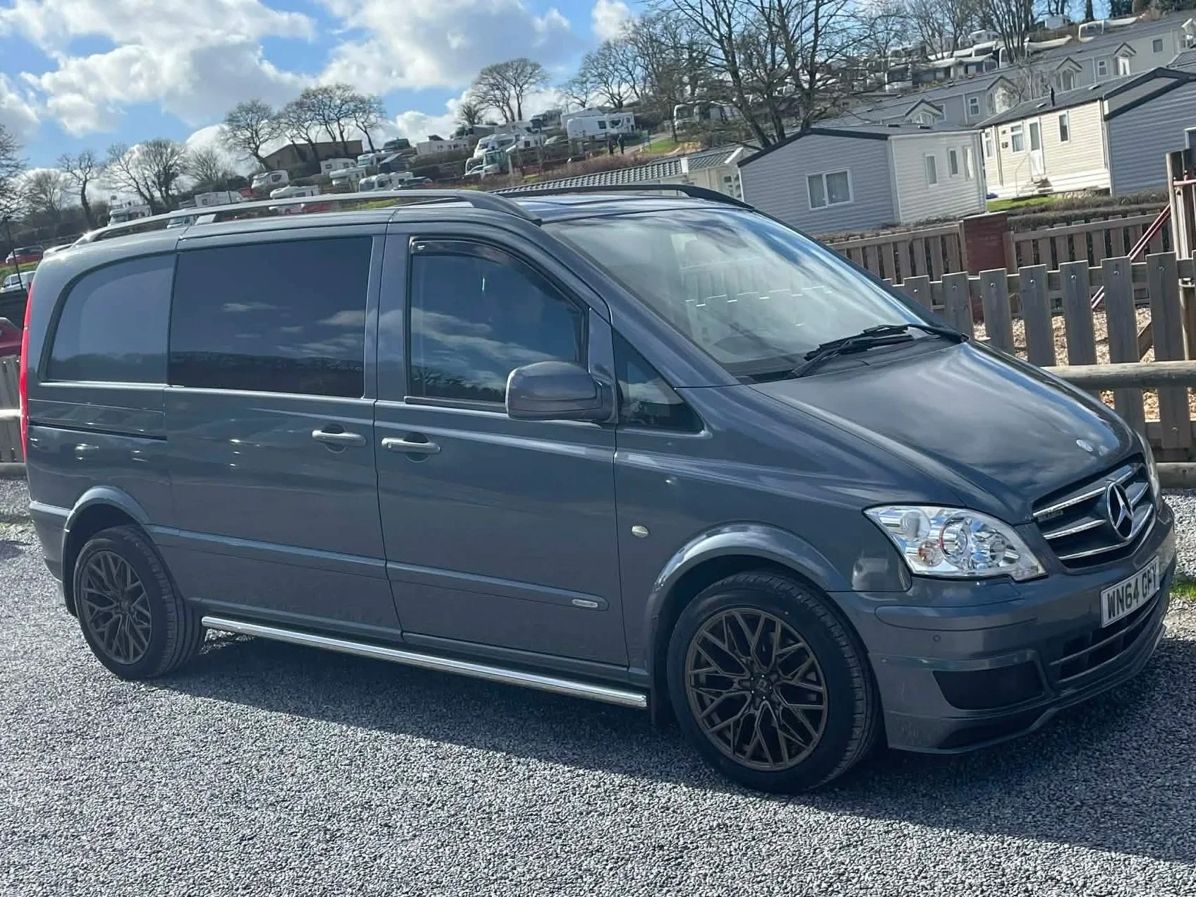 Gray Mercedes-Benz van parked on a gravel drive with houses in the background.