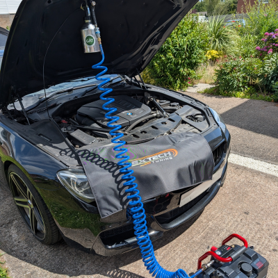 A BMW with the bonnet open is connected to a portable on-vehicle DPF cleaner.
