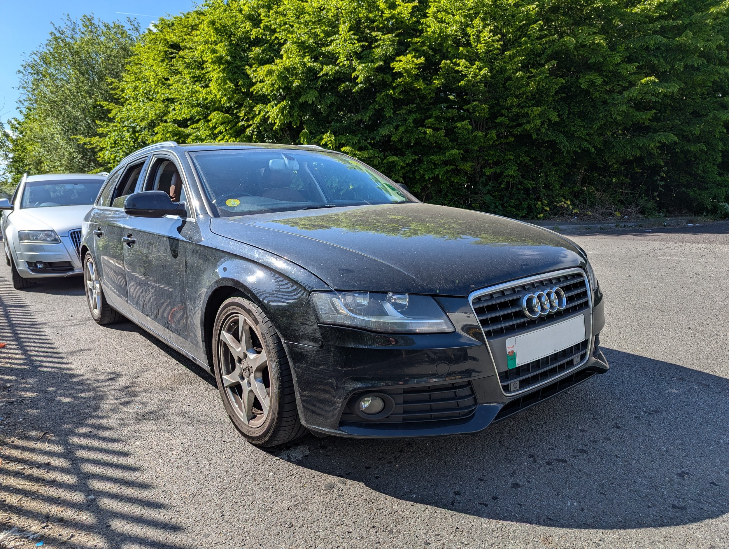 Black Audi A4 car parked on the street with trees in the background.