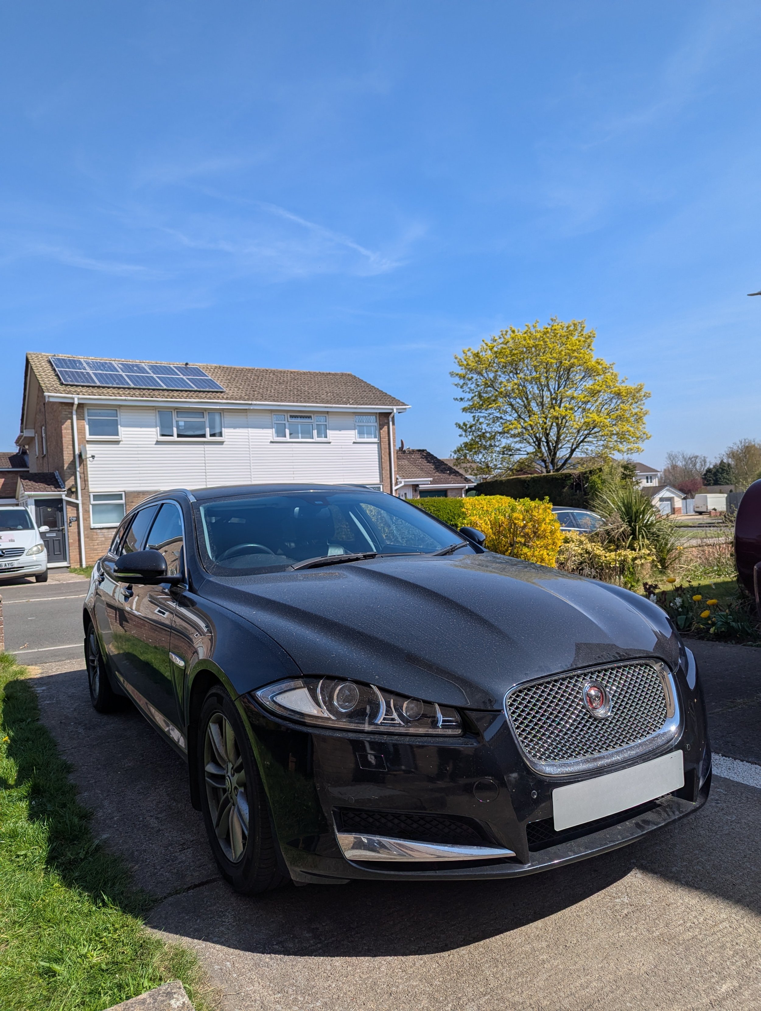 Black Jaguar XF parked on a driveway on a sunny day.