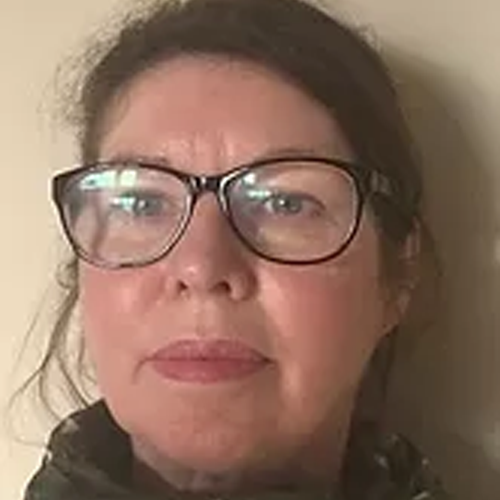 Close-up of a woman with glasses and brown hair, looking at the camera.