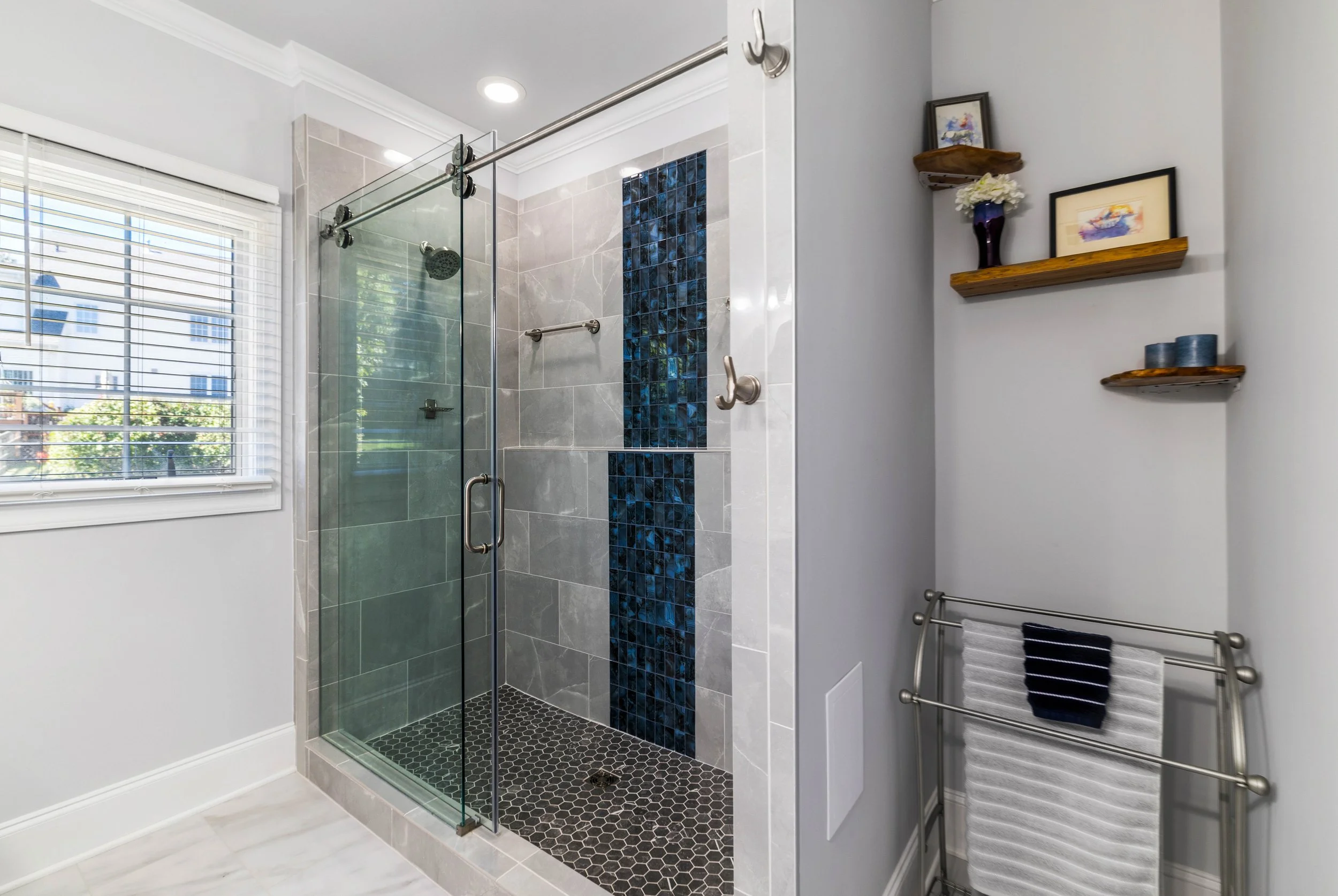 Spacious walk-in shower with gray tile, a Blue Onyx waterfall feature, and a rolling glass door.