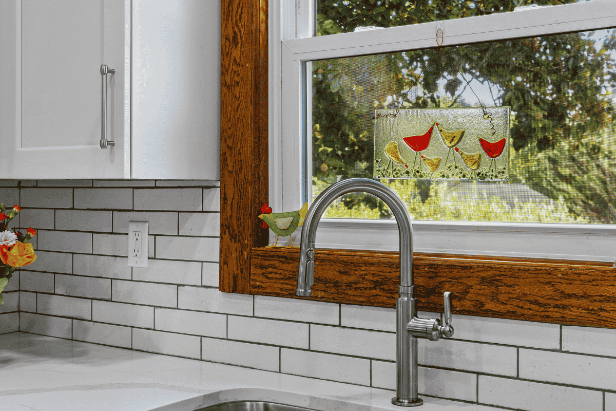 Close-up of tile backsplash with blue and brown flecks beside original stained wood window trim in a renovated Pembroke, Virginia kitchen.