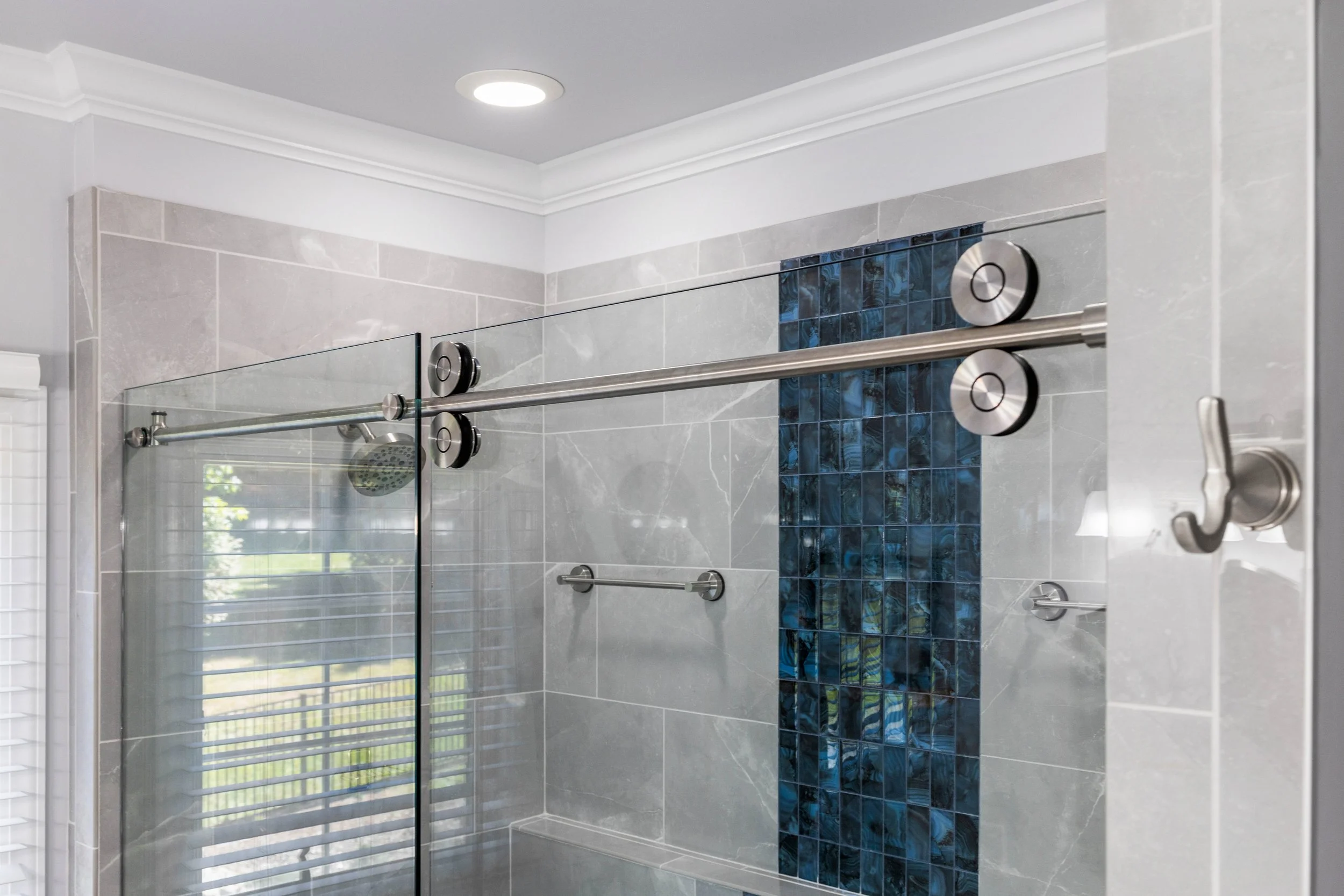 Custom rolling glass shower door with exposed roller hardware and blue accent tile visible through the glass.