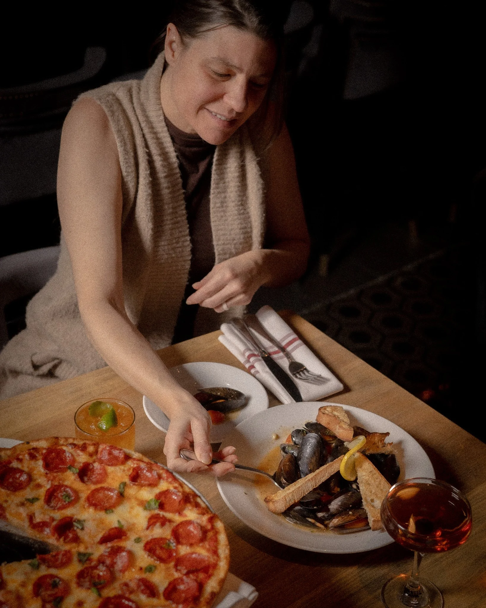 General manager setting a table with mussels, pizza, cocktails, and wine inside The Rossi Kitchen + Bar, highlighting warm hospitality and an intimate dining experience in the Short North.