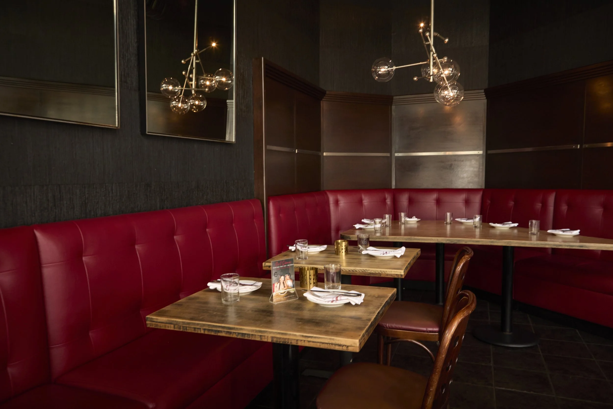 An intimate private dining space at The Rossi Kitchen + Bar with red leather banquettes, wood tables, and modern lighting, ideal for small group celebrations and private dinners.