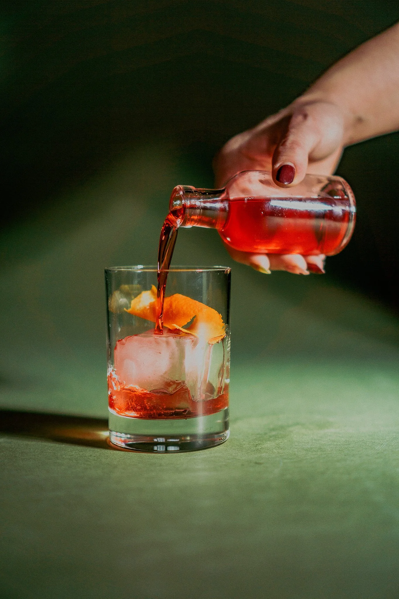 Handcrafted Italian cocktail being poured at The Rossi Kitchen + Bar in Columbus, Ohio, featuring a Negroni-style drink with citrus peel over a large ice cube.