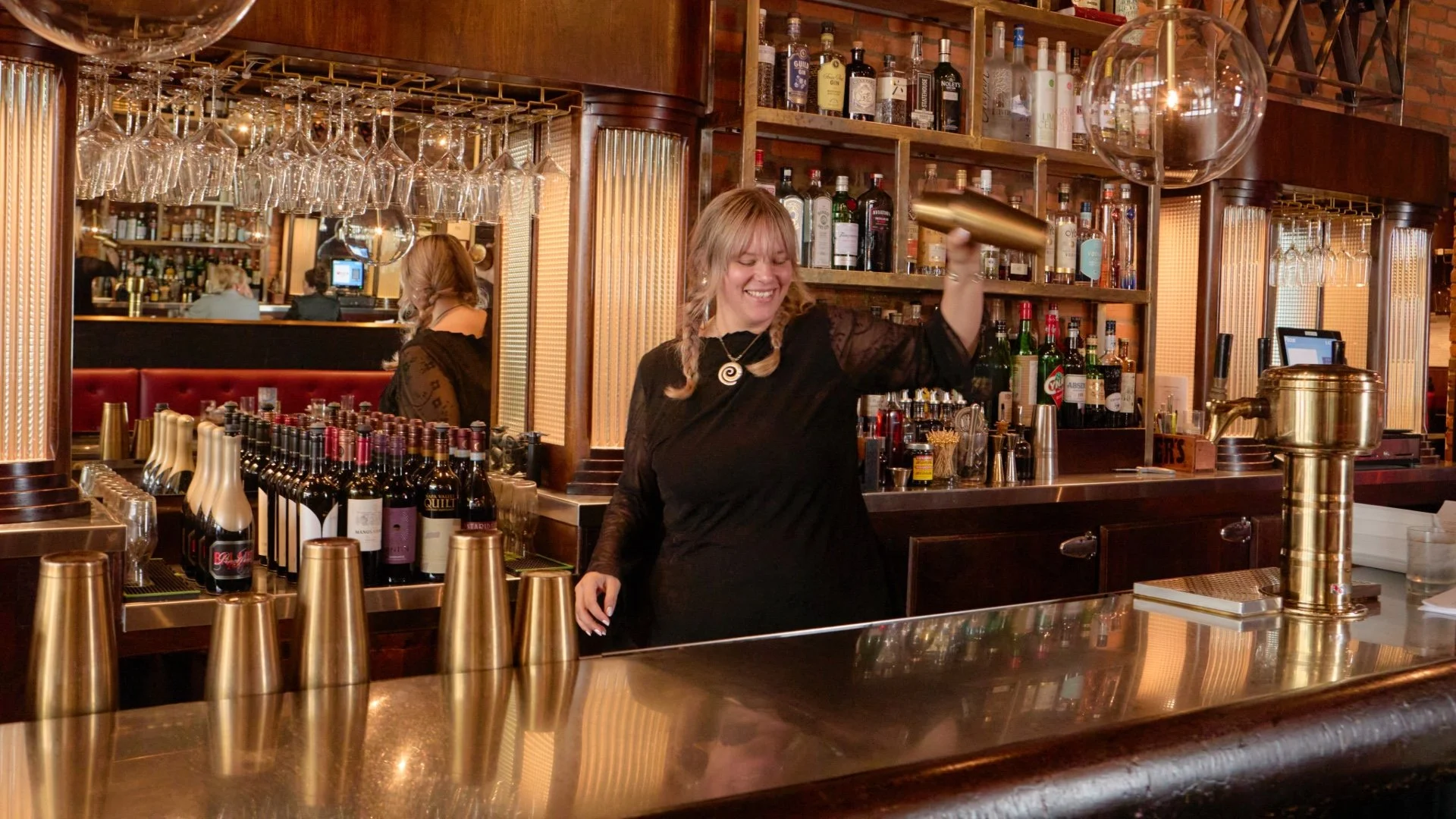 A bartender shaking a cocktail behind the bar at The Rossi Kitchen + Bar, surrounded by shelves of spirits and softly lit glassware, highlighting the restaurant’s elevated cocktail program.