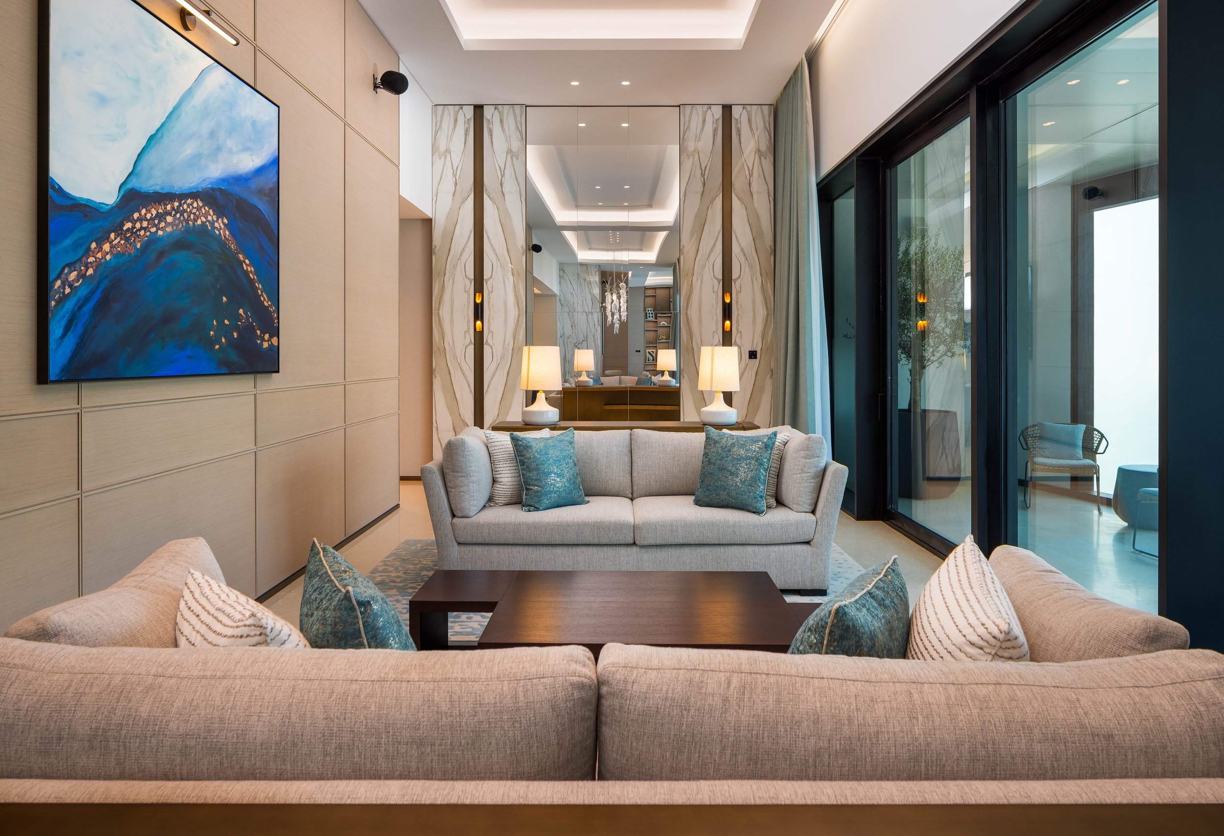 Modern living room with beige sofas, blue pillows, large abstract painting, and glass sliding doors