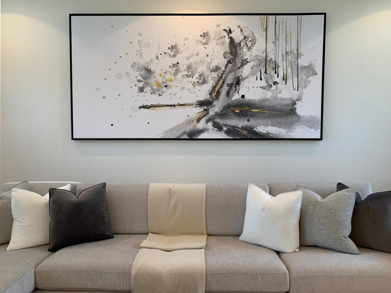 Modern abstract painting above a beige sofa with various pillows