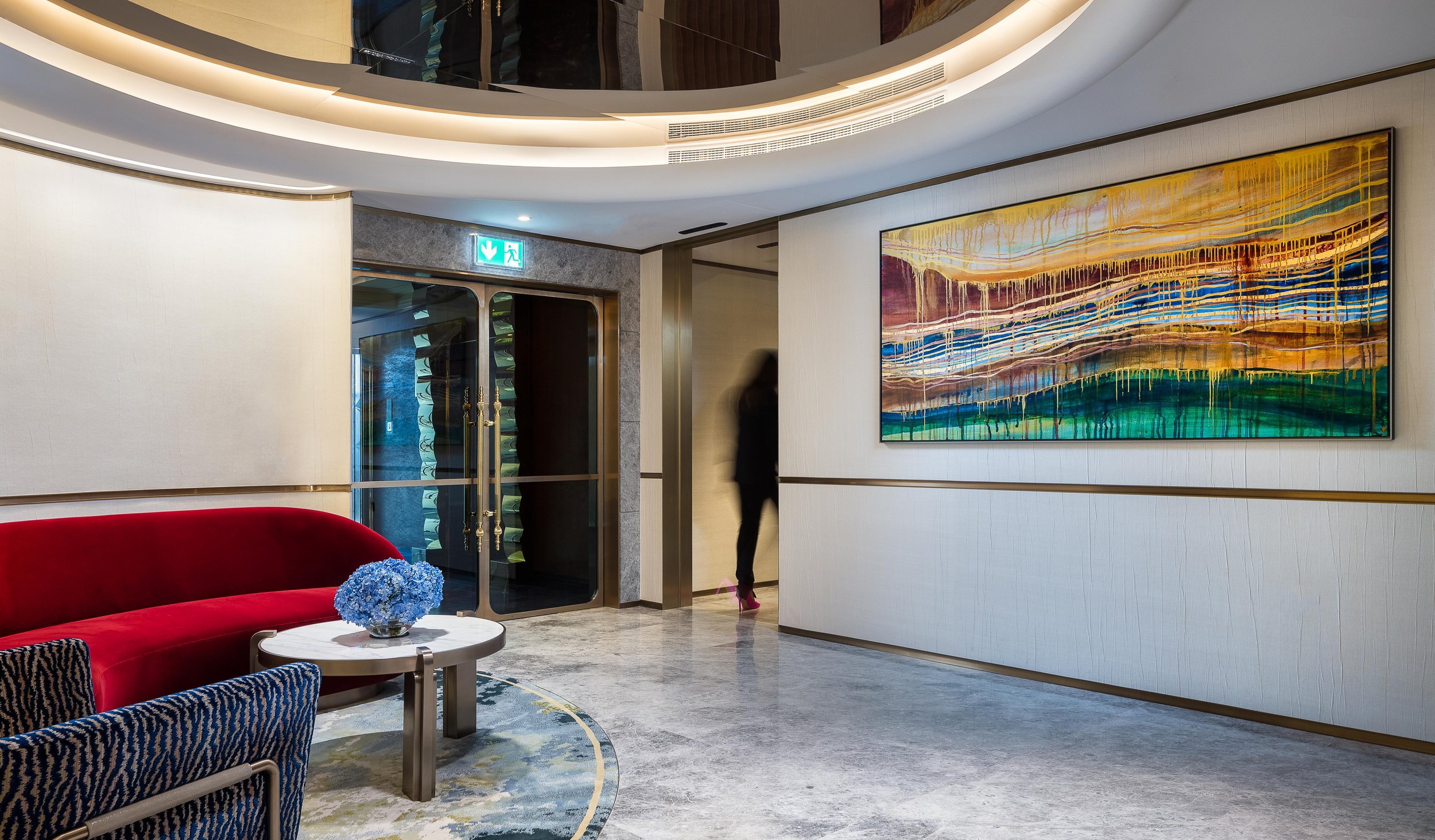 Modern hotel lobby with red couch, abstract painting, blue flower arrangement on a table, and glass doors.