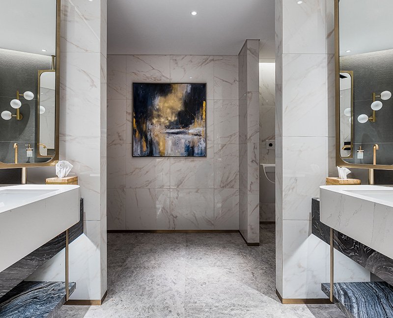 Elegant bathroom with marble walls, abstract painting, dual sinks, and modern fixtures.
