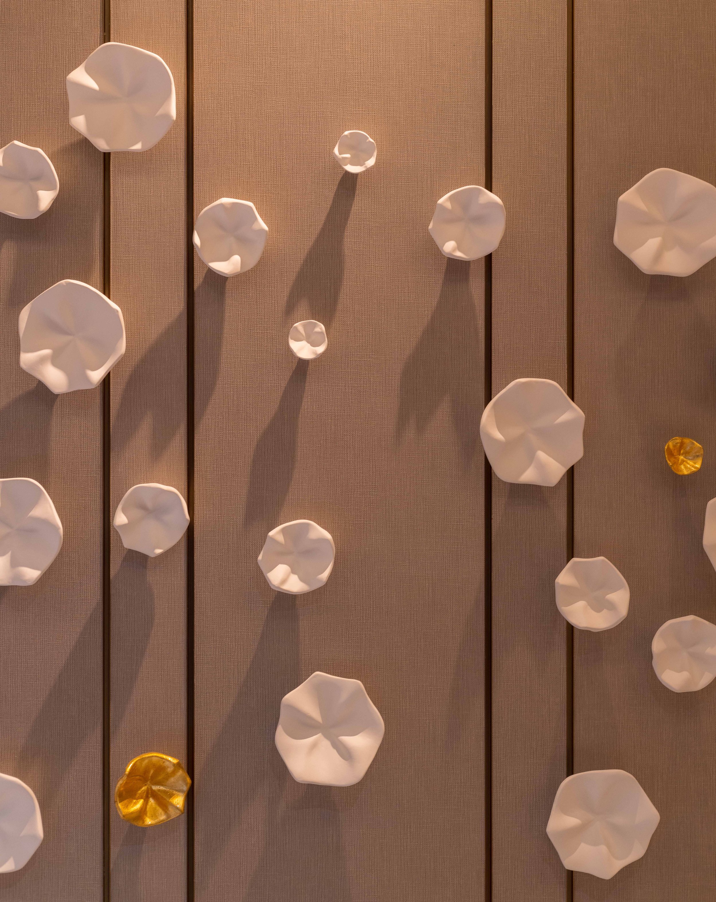 Wall with decorative three-dimensional white and gold flower shapes on a textured beige surface.