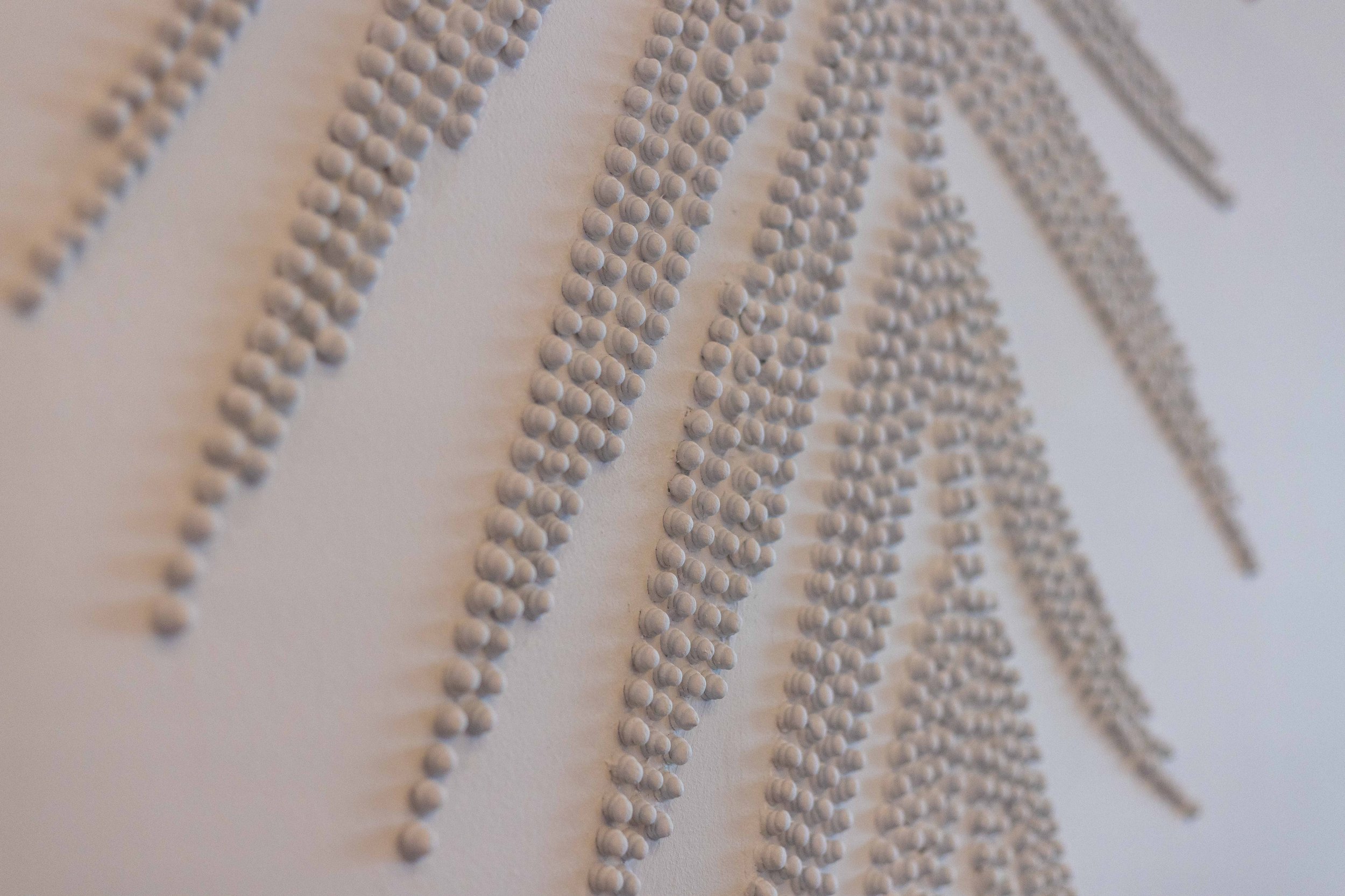 Close-up of abstract wall art made with arranged small white beads forming lines and patterns.