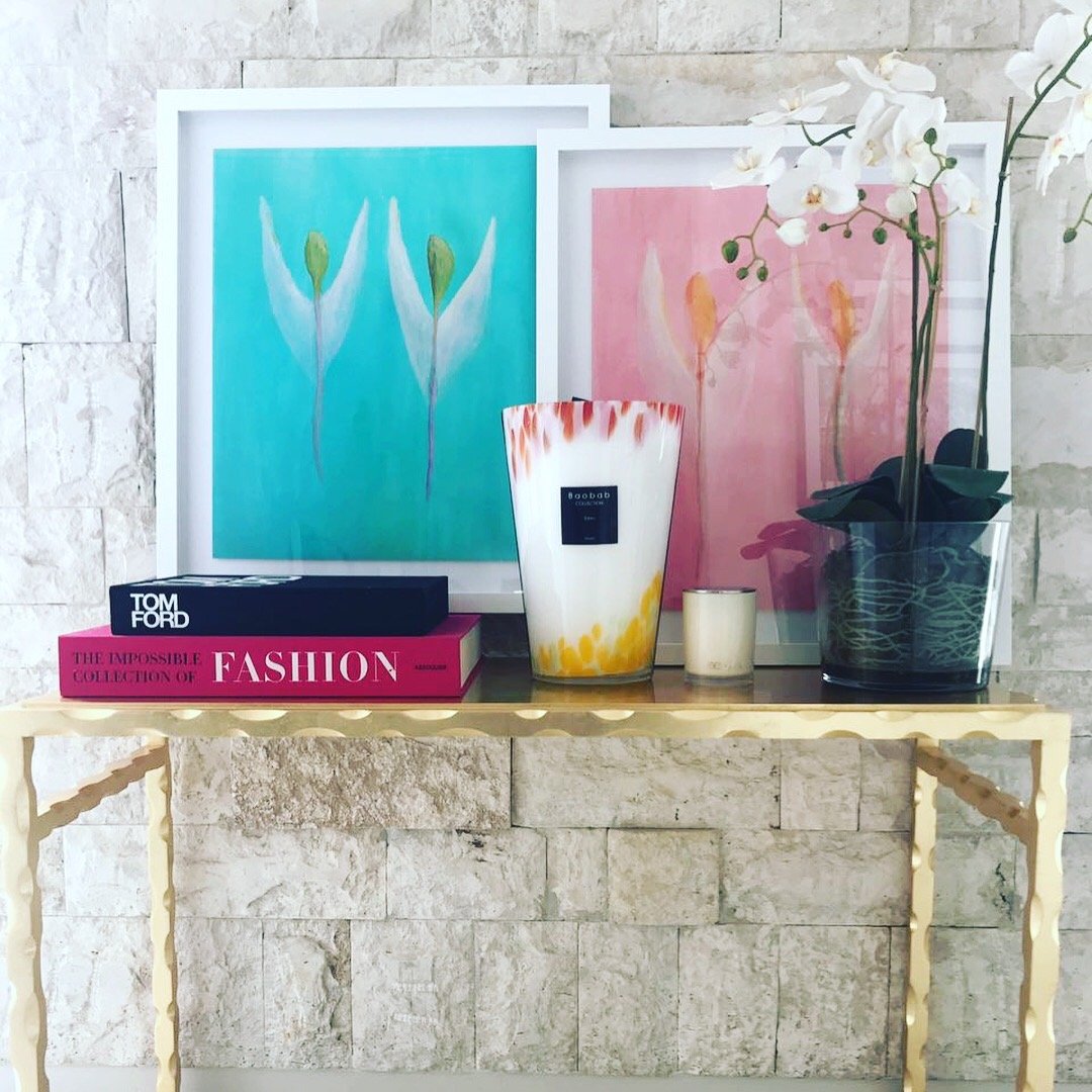 Decorative table with flower paintings, fashion books, candles, and orchid on textured wall