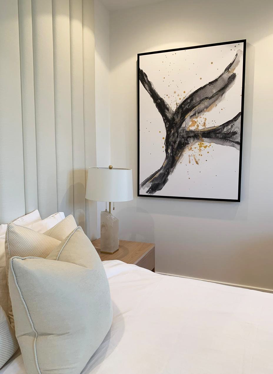 Modern bedroom with abstract painting, white pillows, table lamp, and wooden nightstand.
