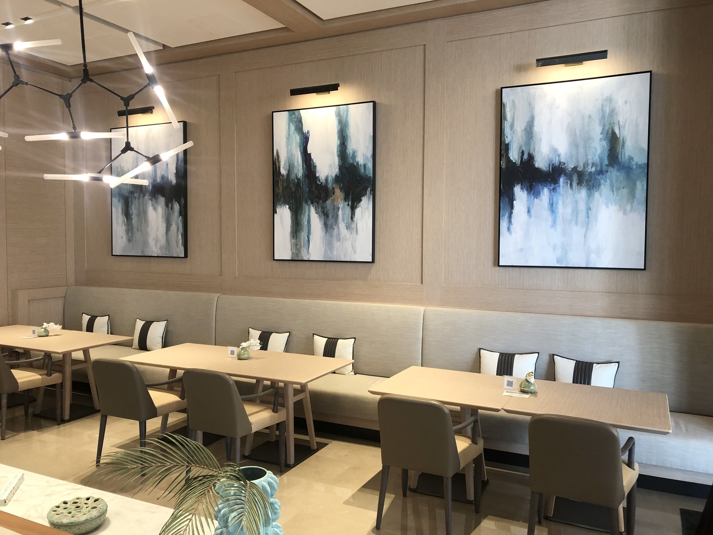 Modern dining area with three abstract paintings, neutral furniture, and geometric chandelier
