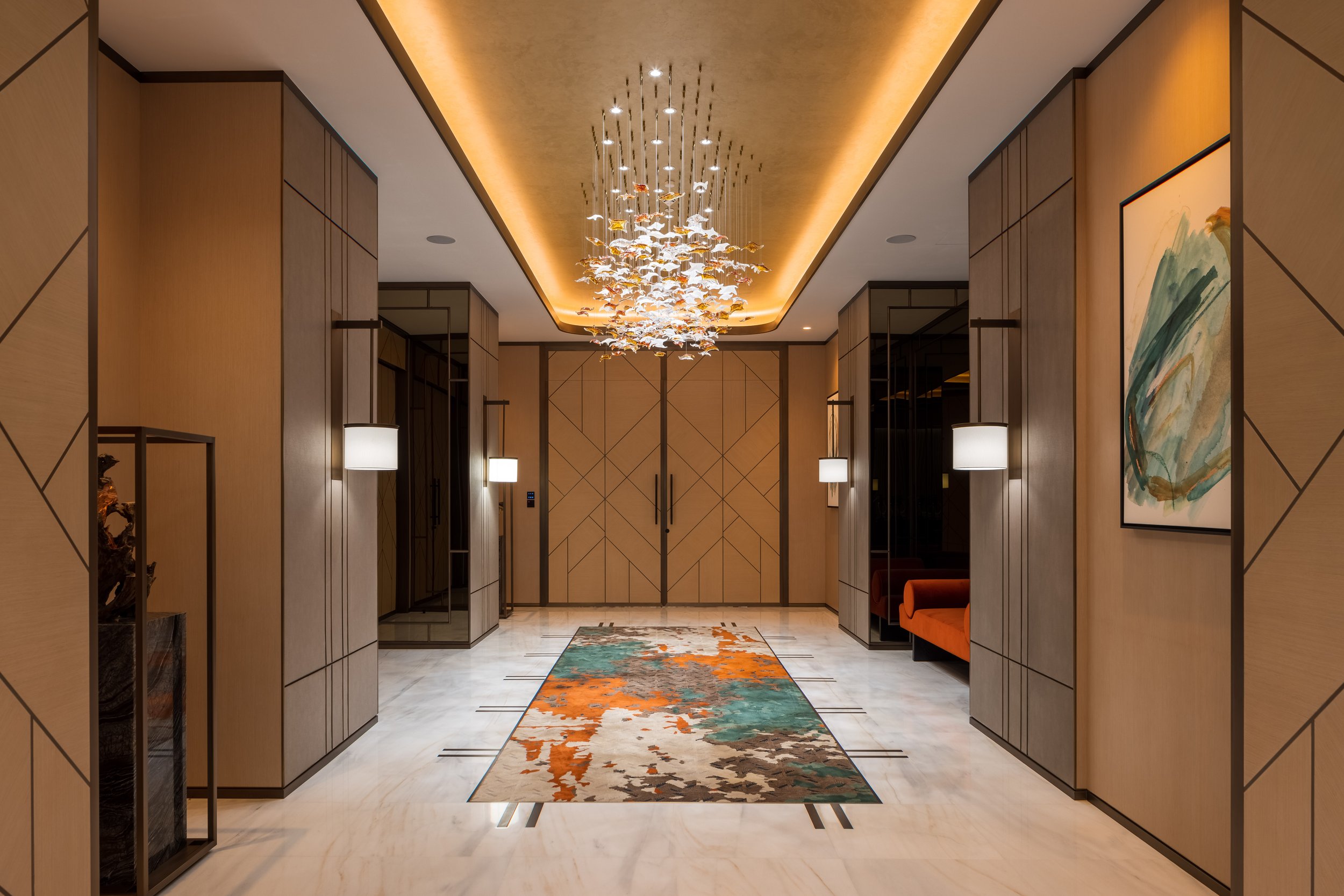 Modern hallway with abstract chandelier, colorful rug, and contemporary artwork.