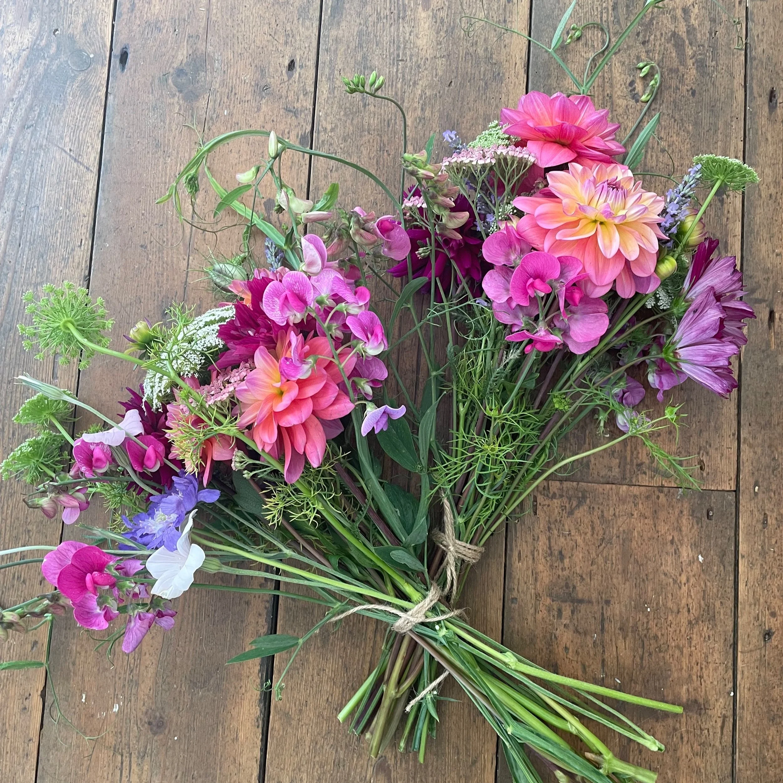 A bouquet of colorful flowers including pink, purple, white, and yellow blooms, tied with a piece of string, placed on a wooden floor.