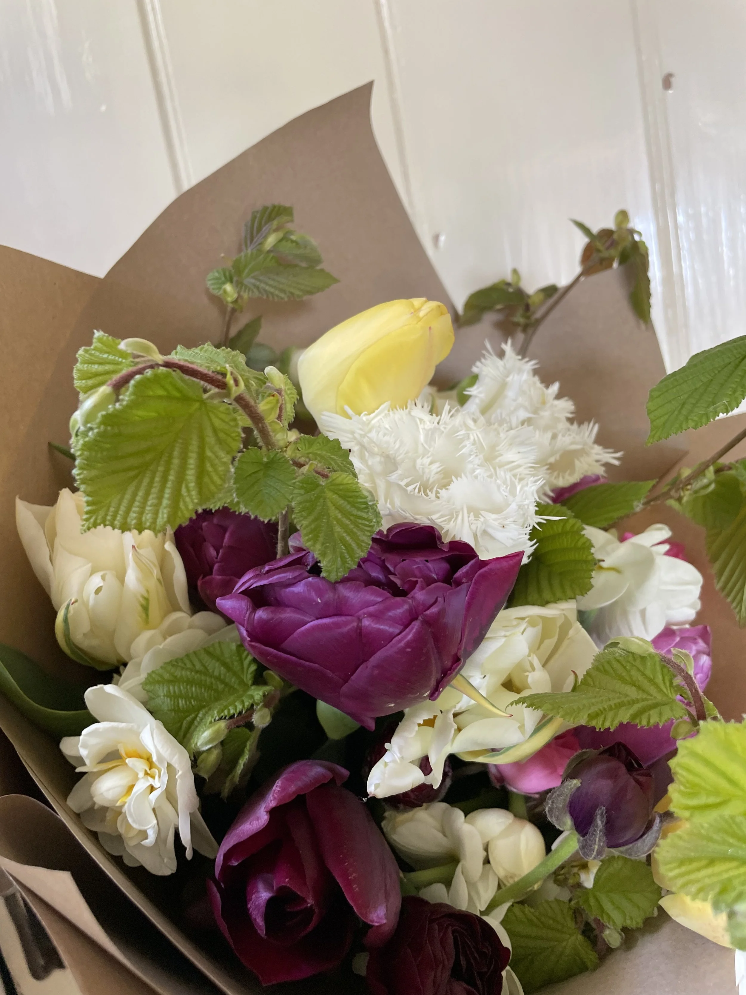Bunch of flowers wrapped in brown paper including pink and purple tulips and white narcissi