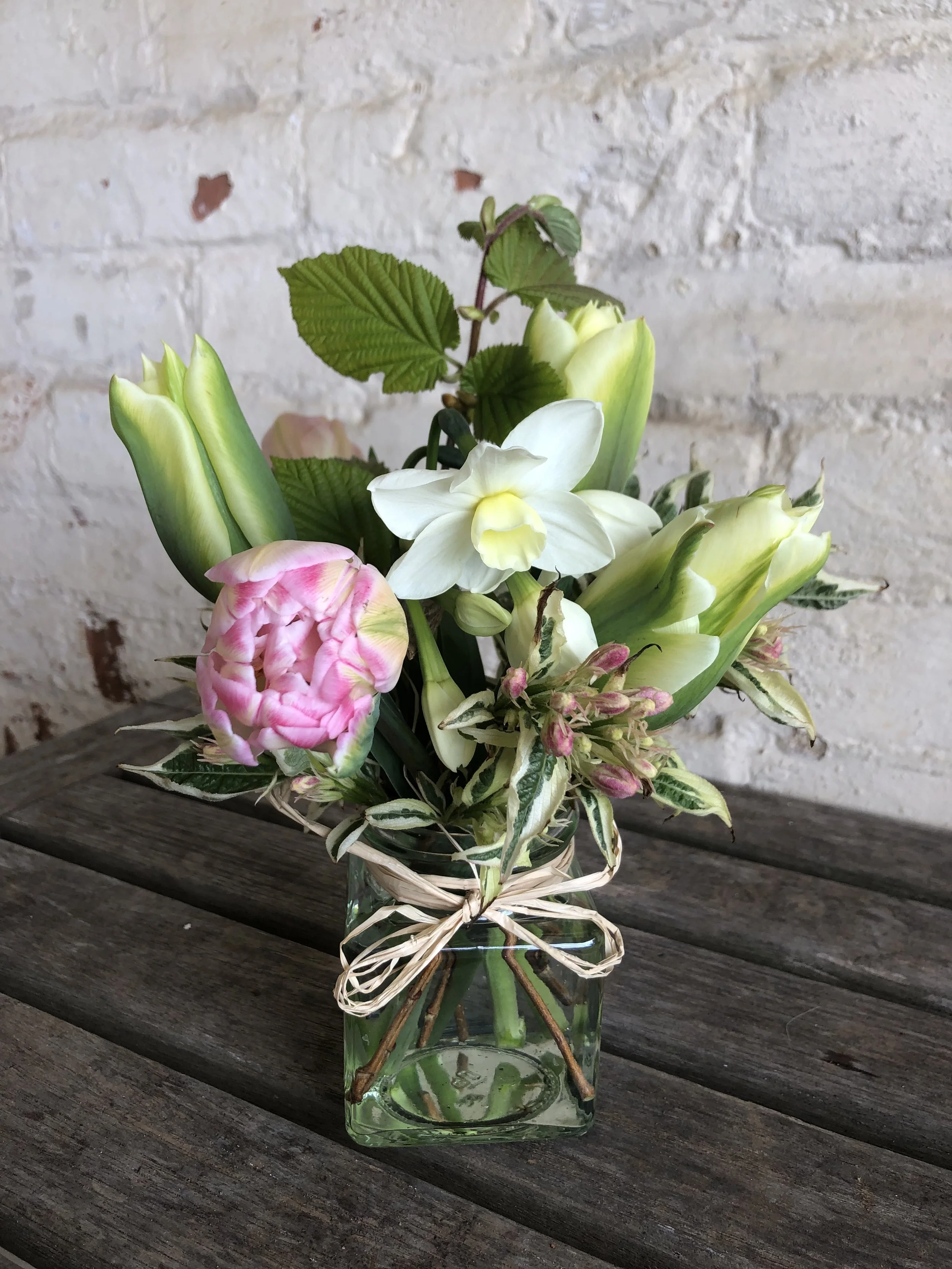 jam jar containing pink and white spring flowers on wooden table with painted brick background