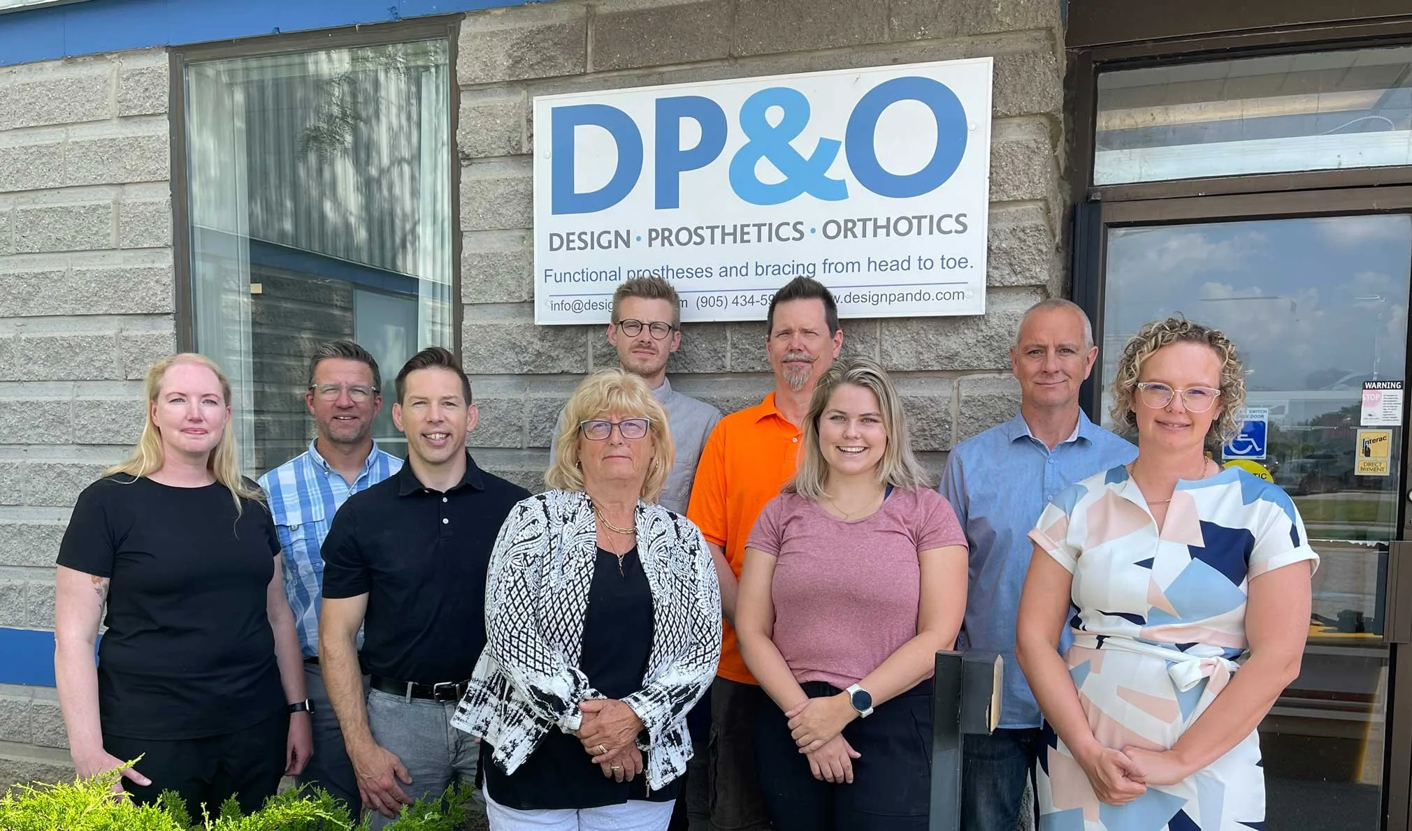 Un groupe de neuf personnes debout devant un bâtiment avec une pancarte indiquant « DP&O Design Prosthetics Orthotics ».