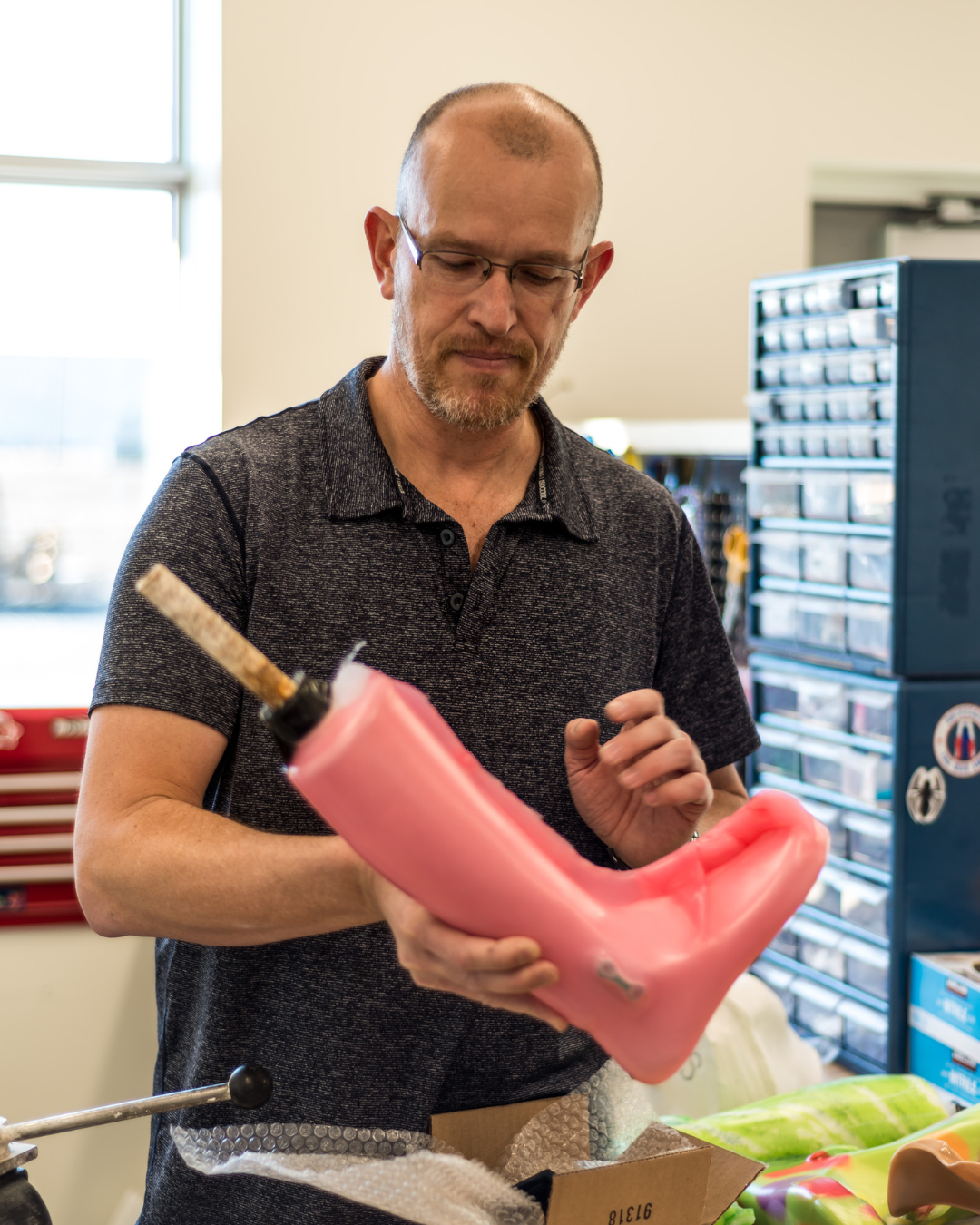 Man inspecting a pink medical or costume prosthetic jaw with a 3D-printed base in a workshop.