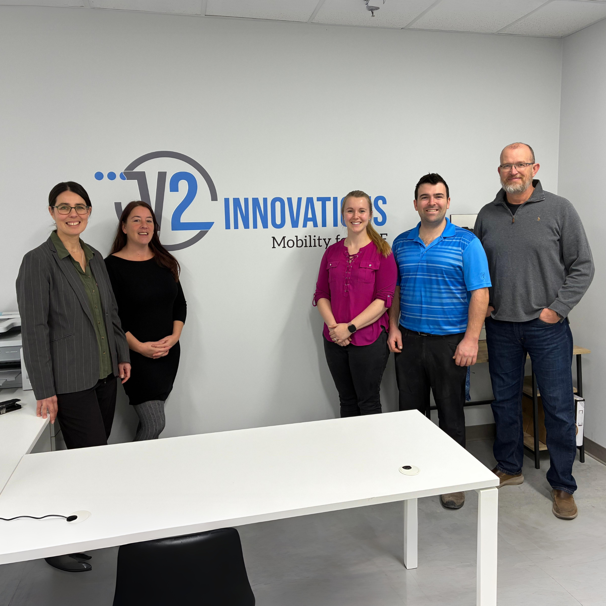 Group of five people standing in front of a wall with a logo and the words 'W2 INNOVATIONS Mobility for All' in an office setting.