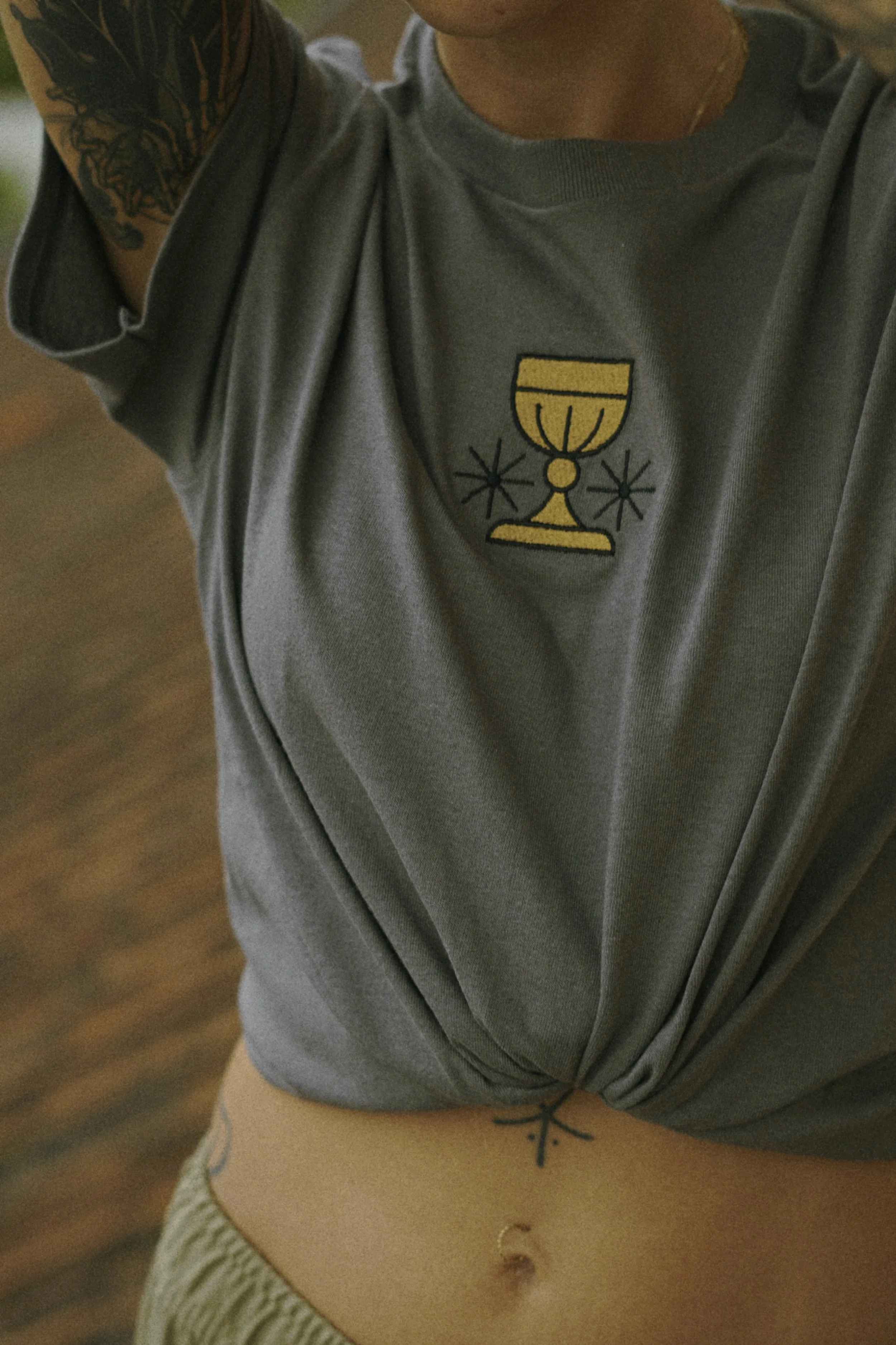 Nahaufnahme eines Tattoos auf einem Arm und auf dem Bauch einer Person, die eine graue T-Shirt trägt.