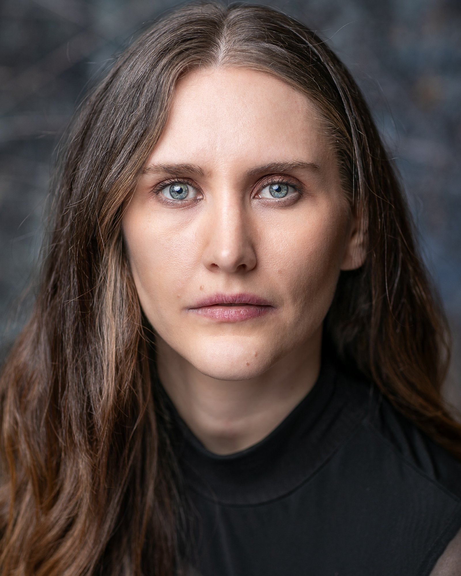 Close-up portrait of a person with long brown hair, blue eyes, wearing a black shirt.