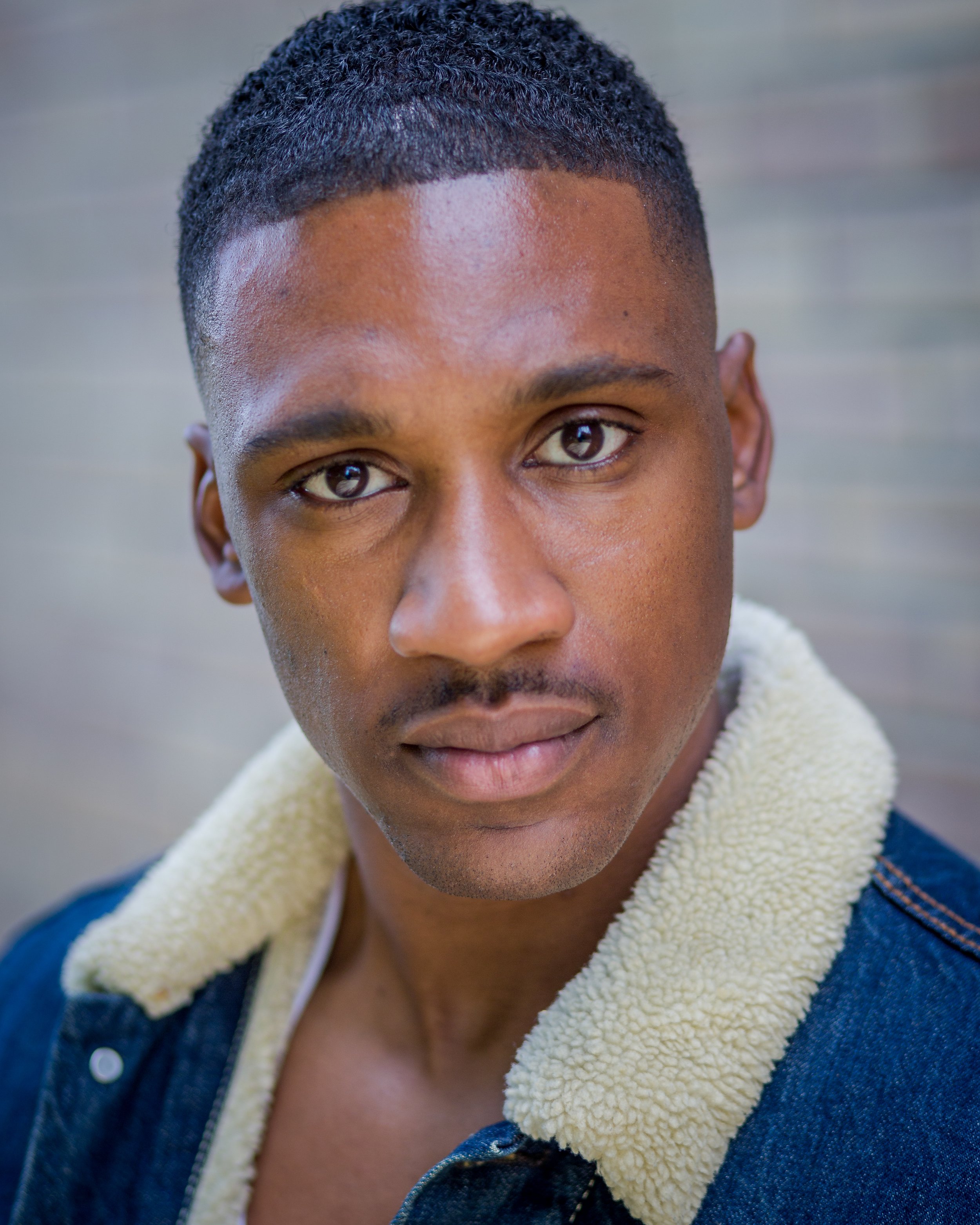 Close-up portrait of a person with short hair wearing a denim and shearling jacket.