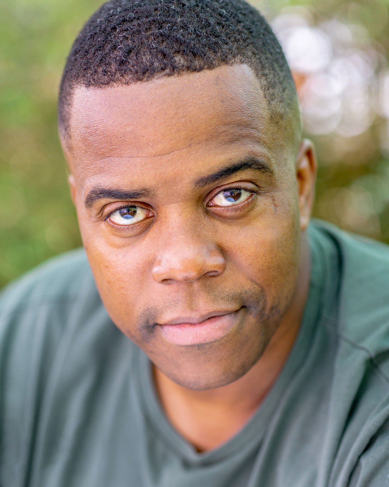 Close-up of a man looking directly at the camera against a blurred green background.