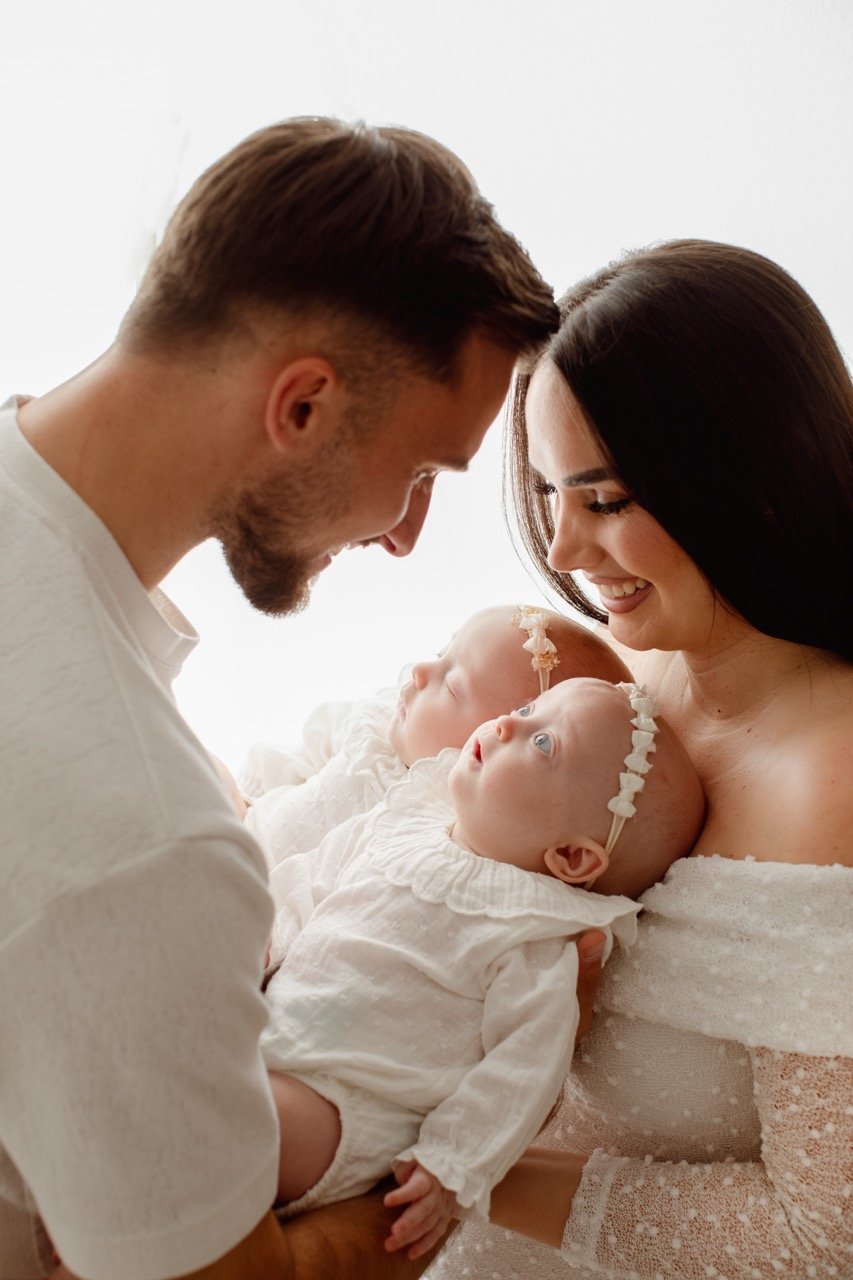 Ein Mann und eine Frau halten liebevoll zwei Babys in weißen Kleidern.