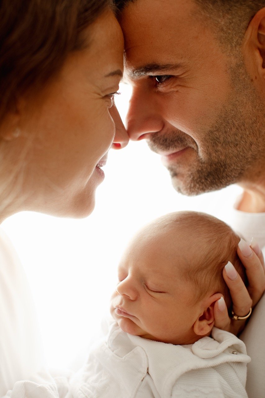 Ein Mann und eine Frau lächeln sich an, während sie ein schlafendes Baby in den Armen halten.