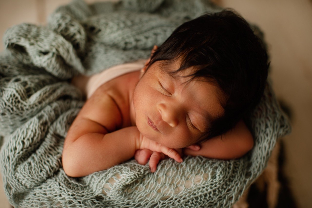 Schlafendes Baby in eine grüne, gestrickte Decke eingewickelt.