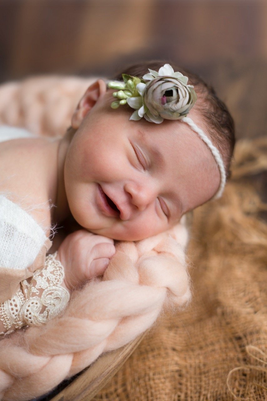 Schlafendes Baby mit Blumenstirnband auf kuscheligem Stoff.