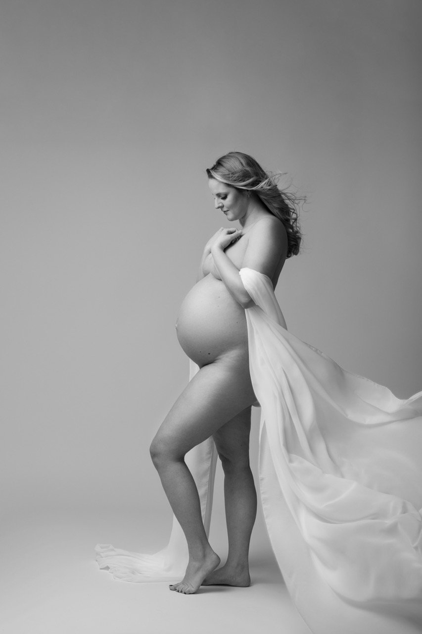 Schwarz-Weiß-Fotografie einer schwangeren Frau, die in ein fließendes Tuch gehüllt ist.